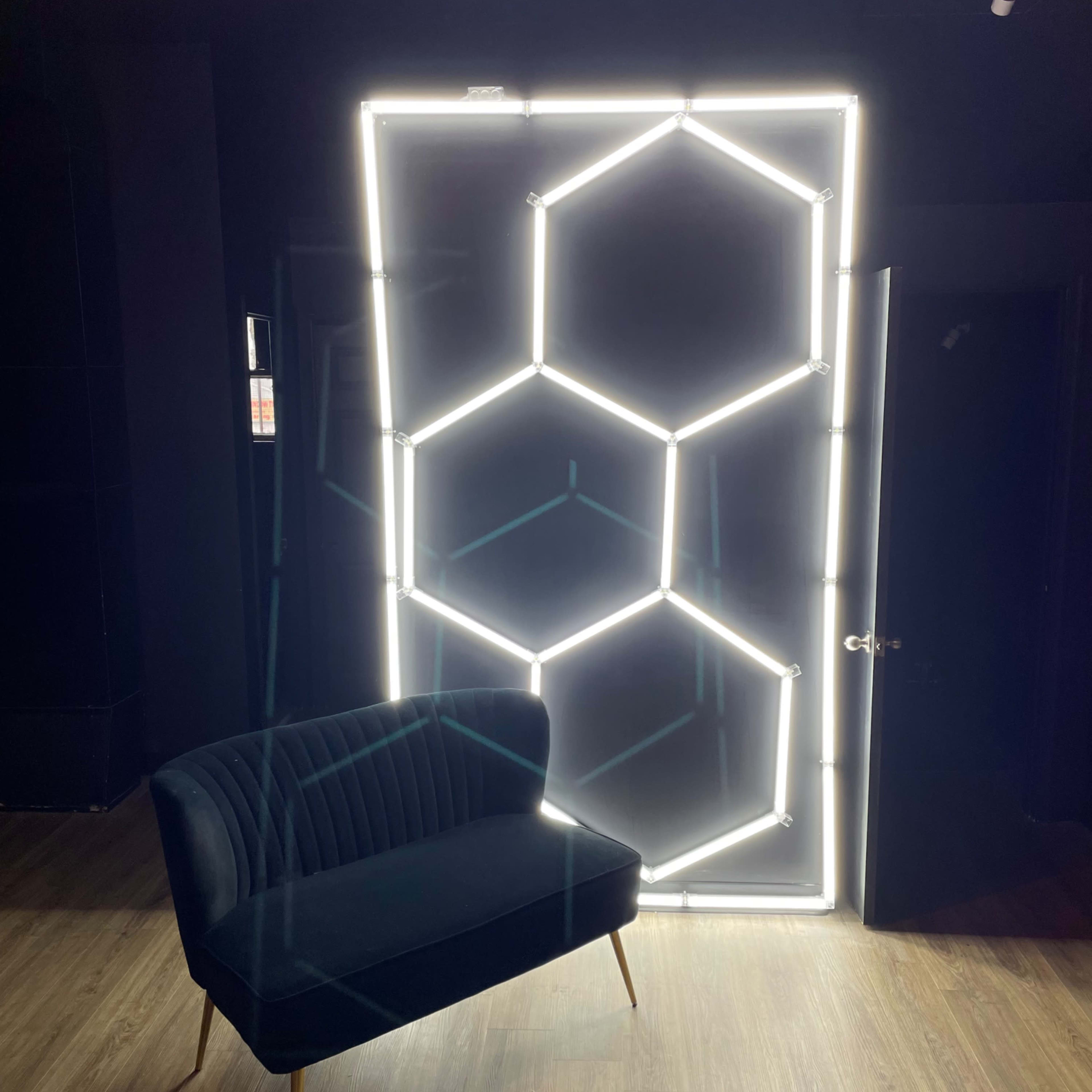A modern black velvet sofa is positioned in front of a glowing hexagon-patterned light installation against a dark wall.