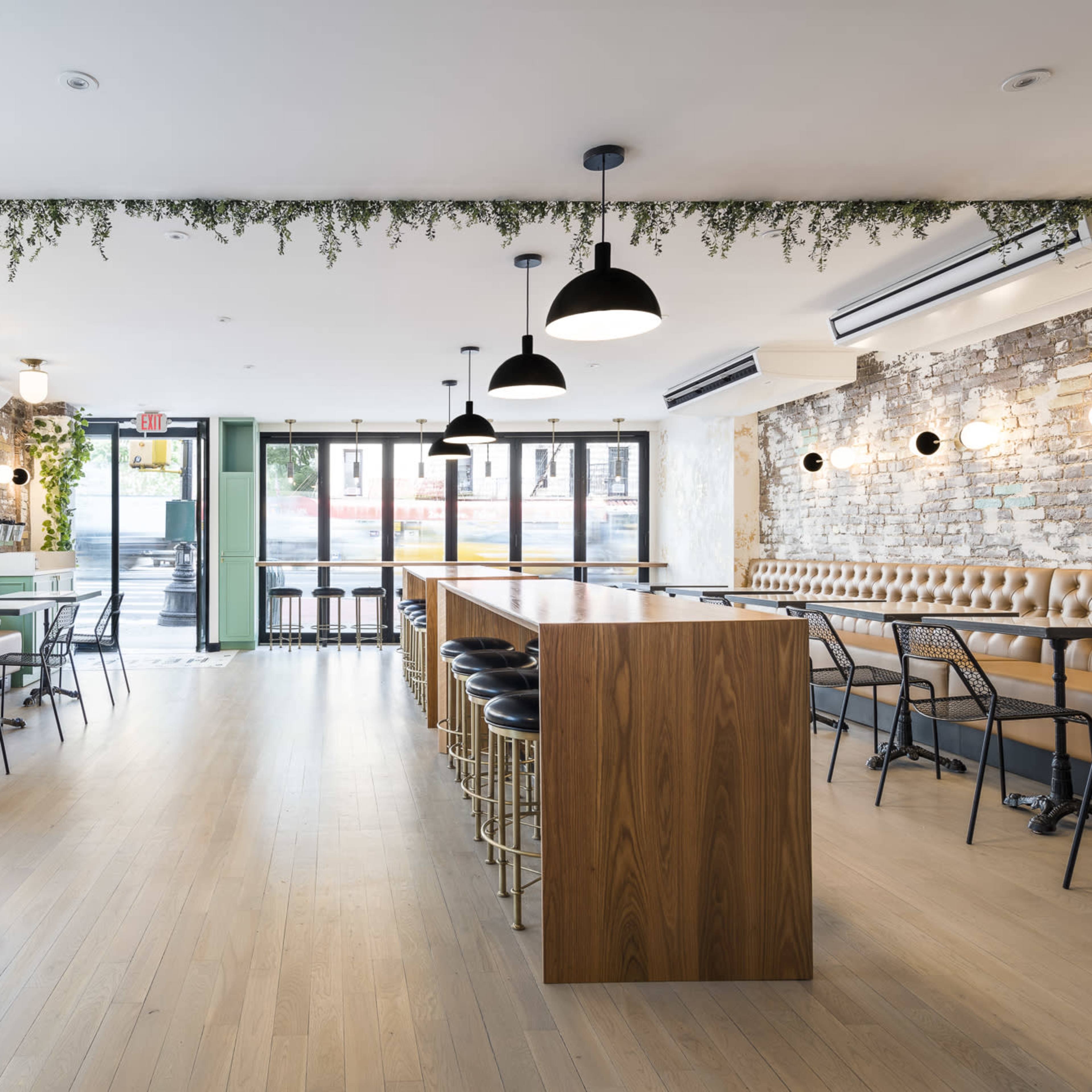 A modern café interior with wooden tables, a long central bar, and large windows allowing natural light to enter.