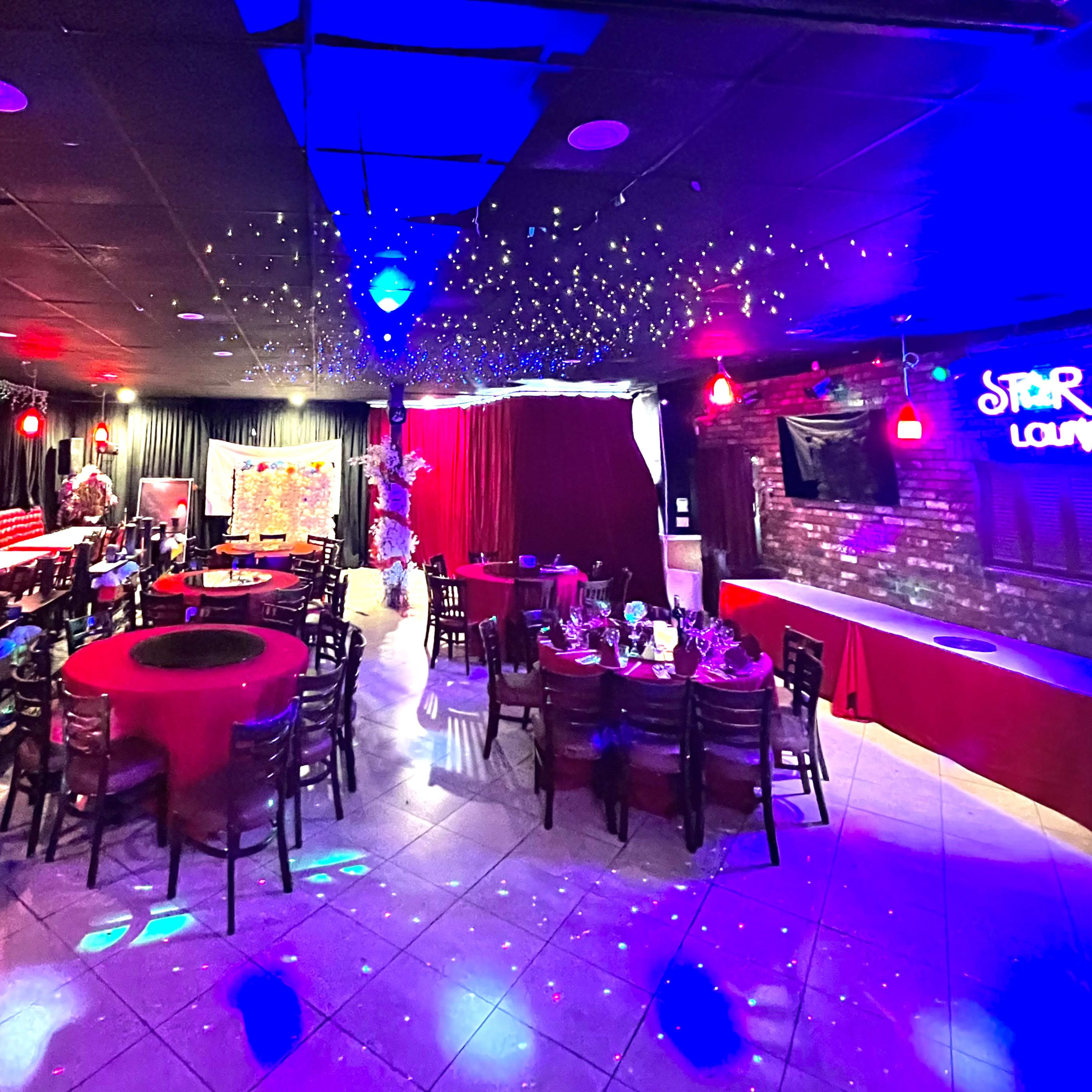 The scene features a vibrant lounge with tables set for an event, illuminated by colored lights and decorated with festive elements.