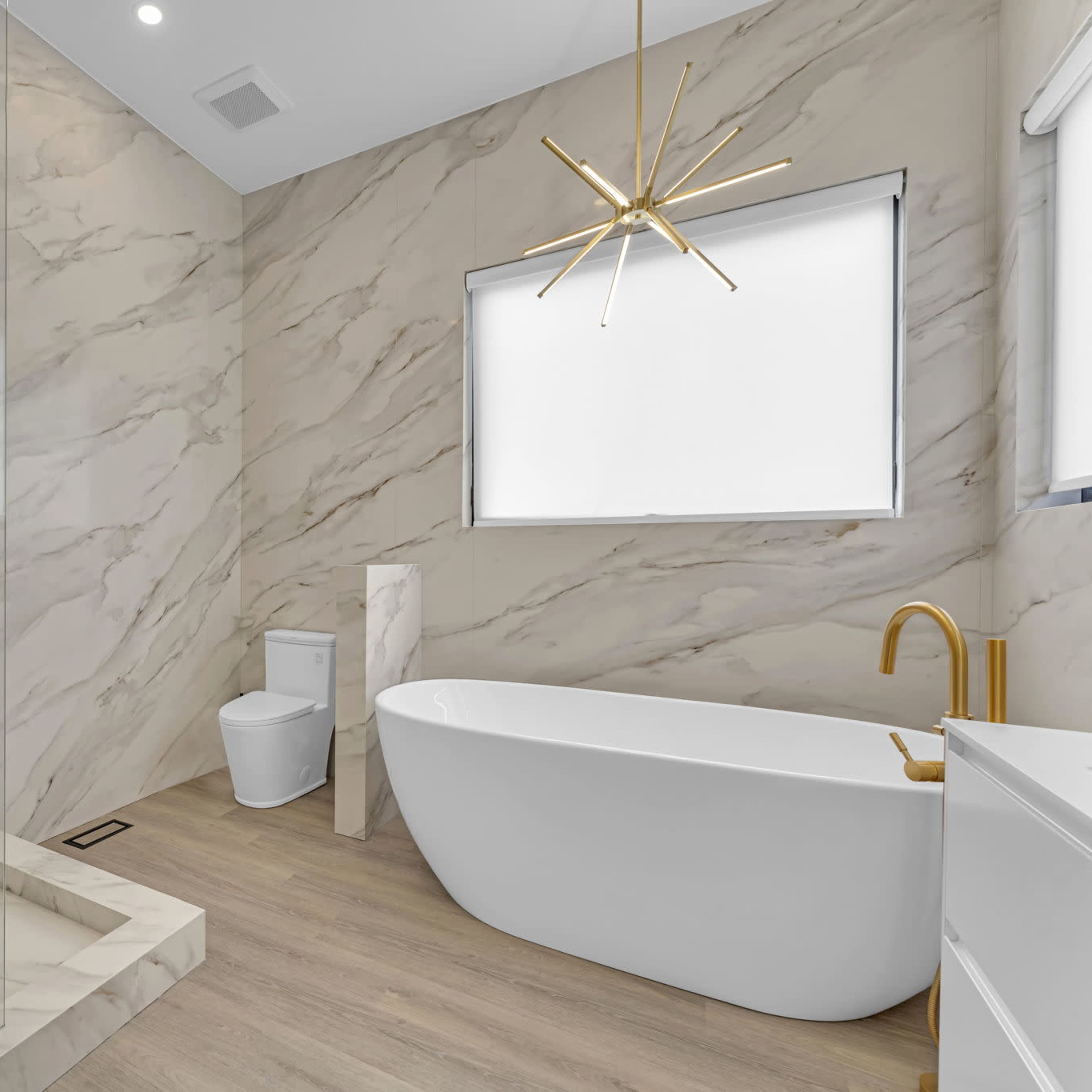 A modern bathroom featuring a freestanding bathtub, a shower area with clear glass, a toilet, and a wall adorned with marble-patterned tiles.