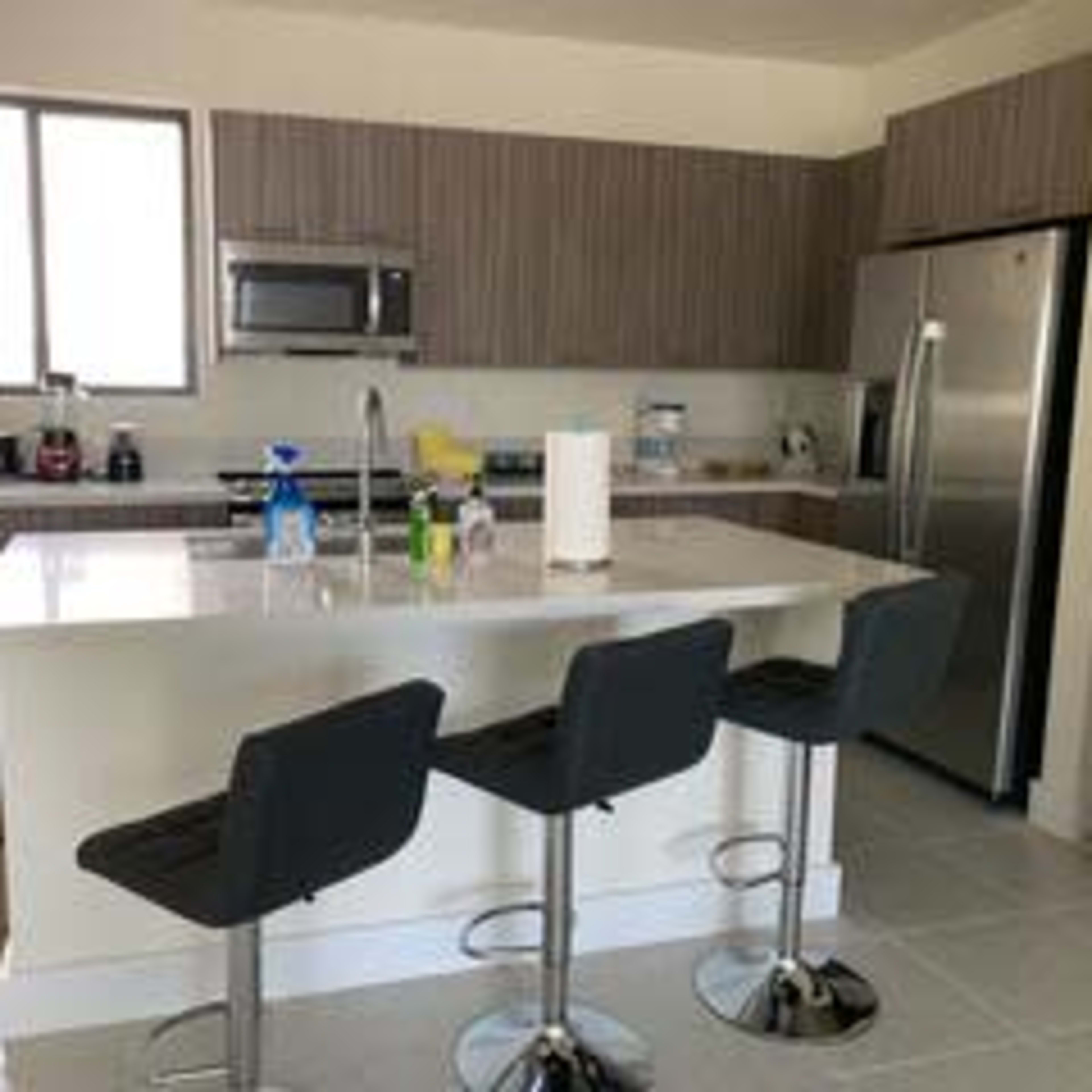 A modern kitchen features gray cabinetry, stainless steel appliances, and a central island with three black bar stools.