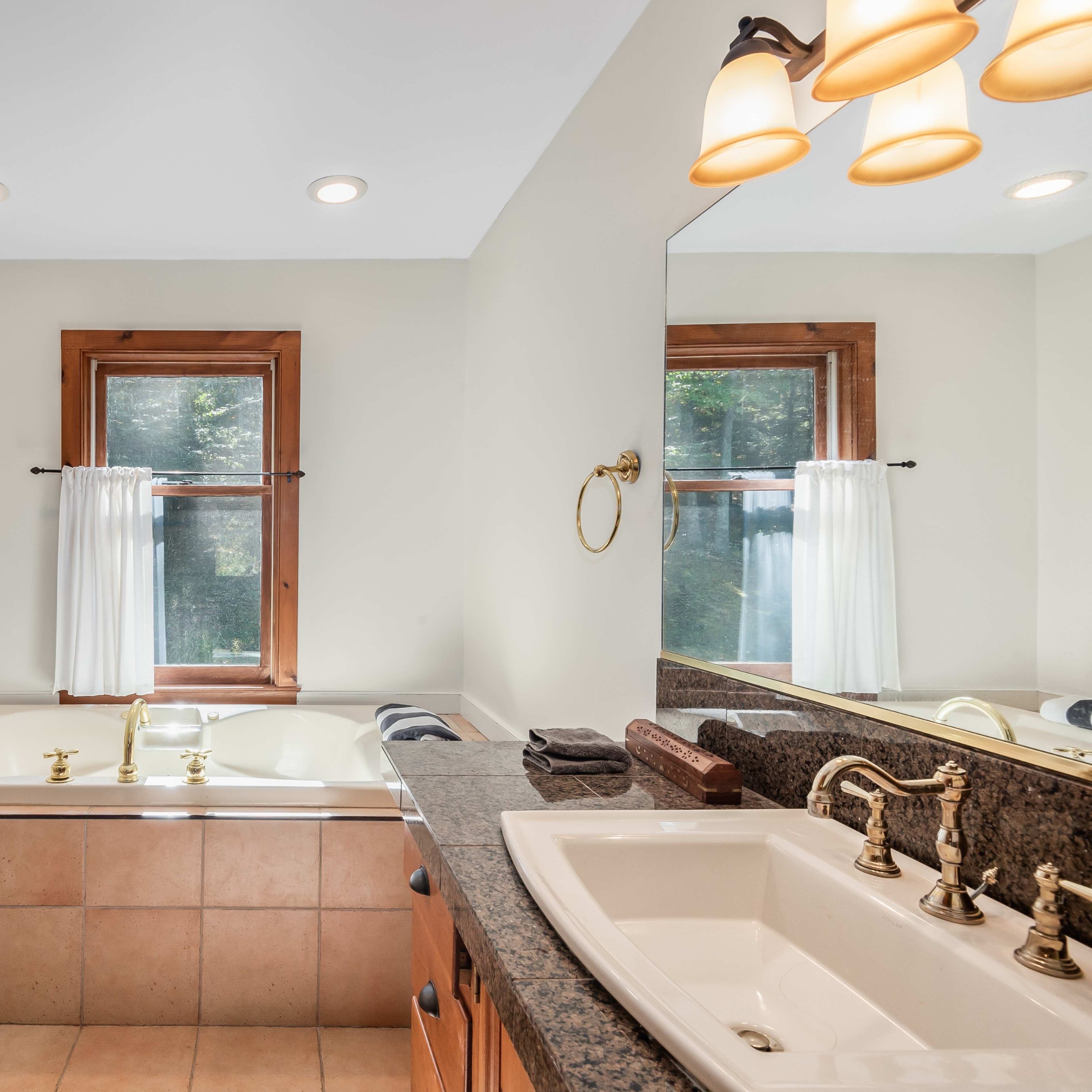 The bathroom features a large bathtub next to a window, a double sink vanity with dark countertops, and a wooden door.