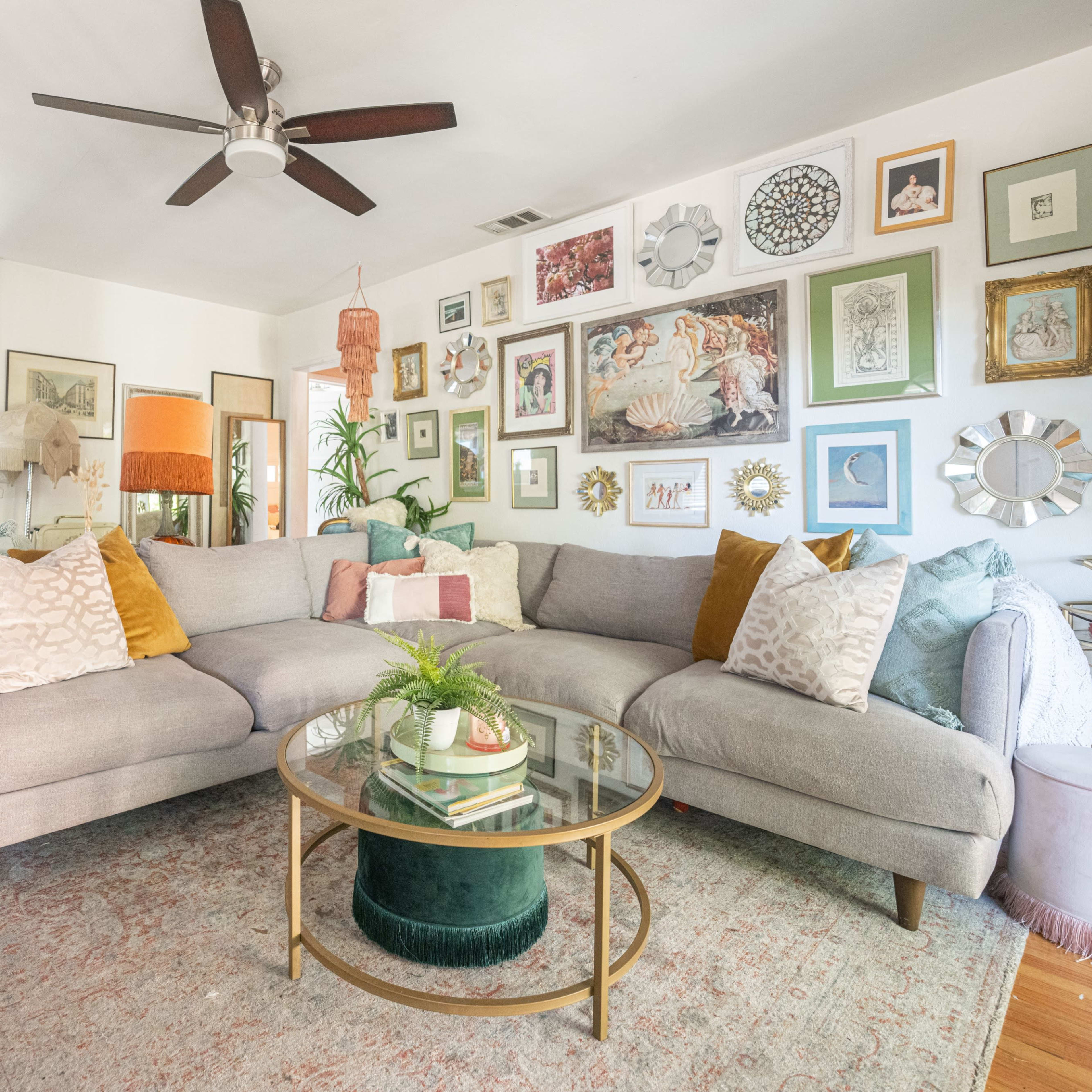 A modern living room with a large gray sectional sofa, a glass coffee table, and various framed artworks arranged on the wall.