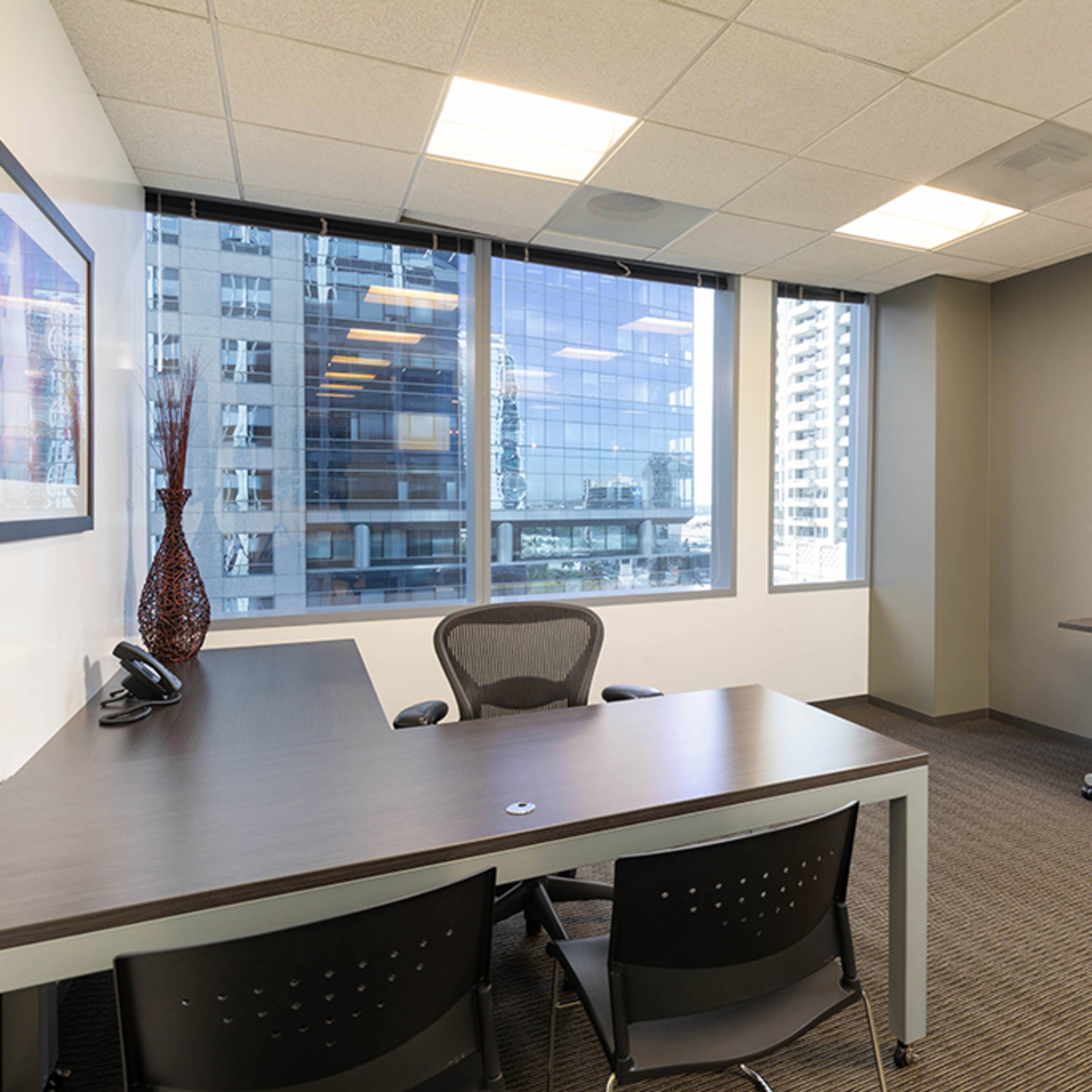 A sleek office space with a large desk, two chairs, and large windows overlooking a cityscape.