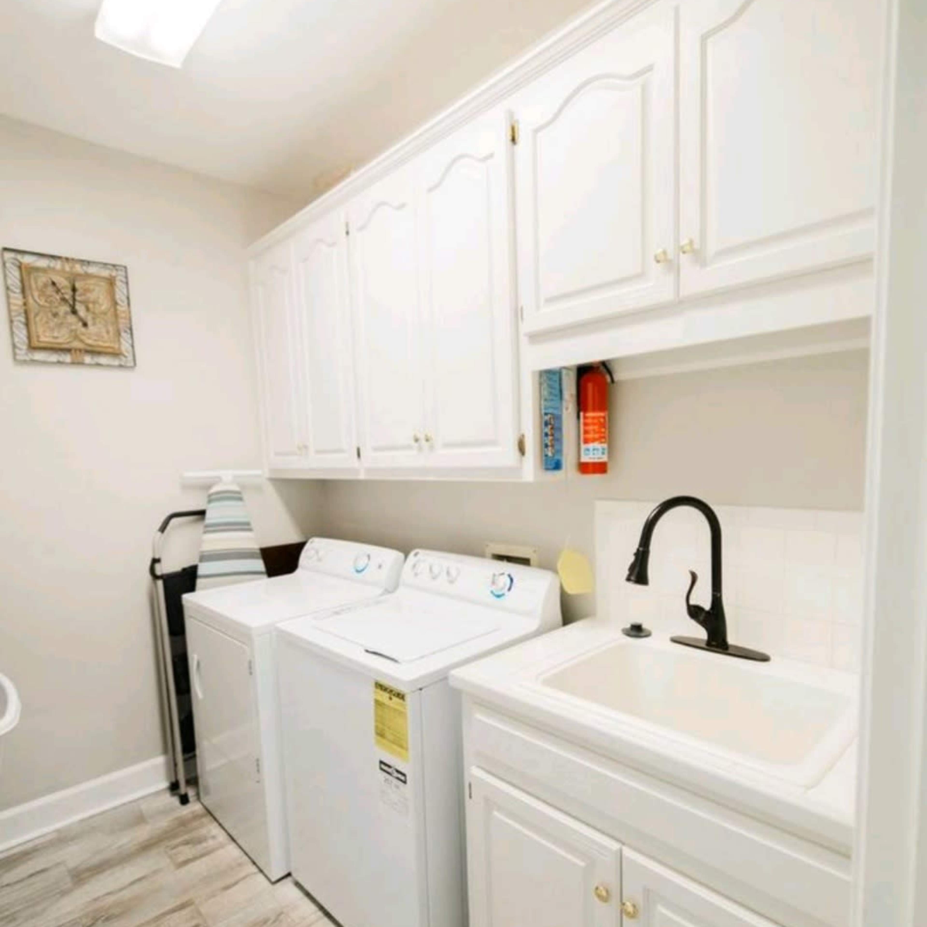 A laundry room with white cabinetry, a washing machine, a dryer, and a sink.
