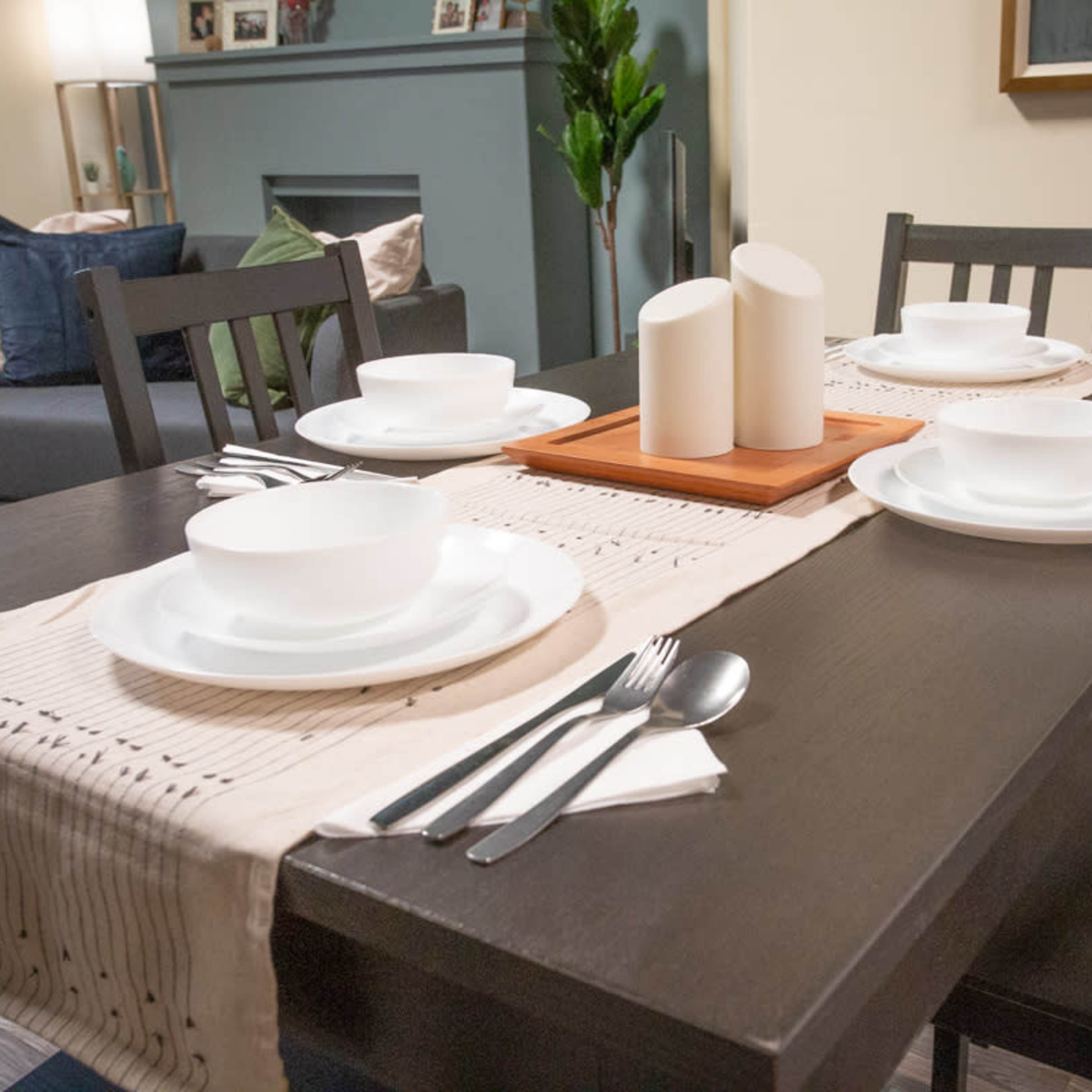 A dining table is set with white plates and utensils, accompanied by decorative candles and a table runner.