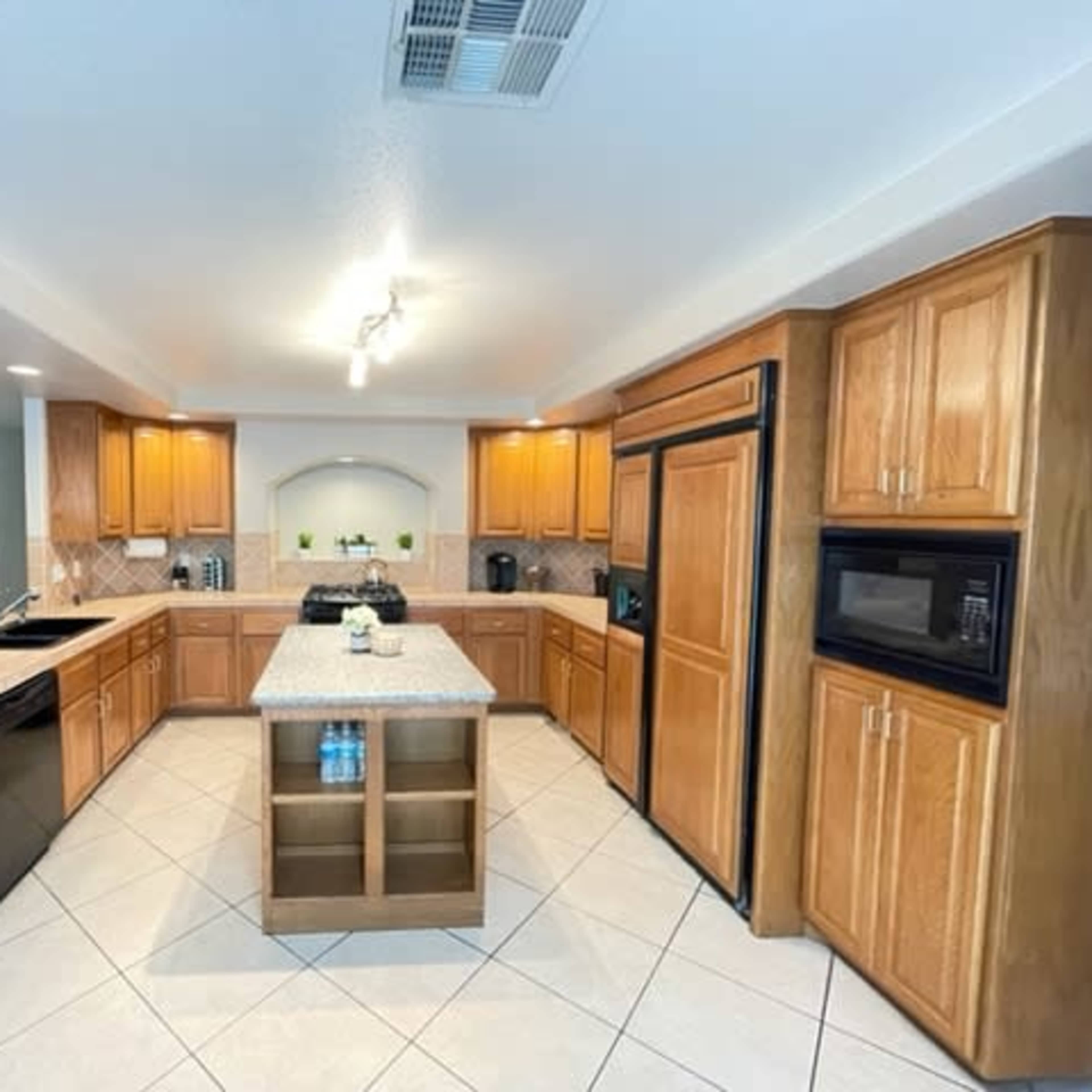 A modern kitchen with wooden cabinetry, a central island, and tiled flooring.
