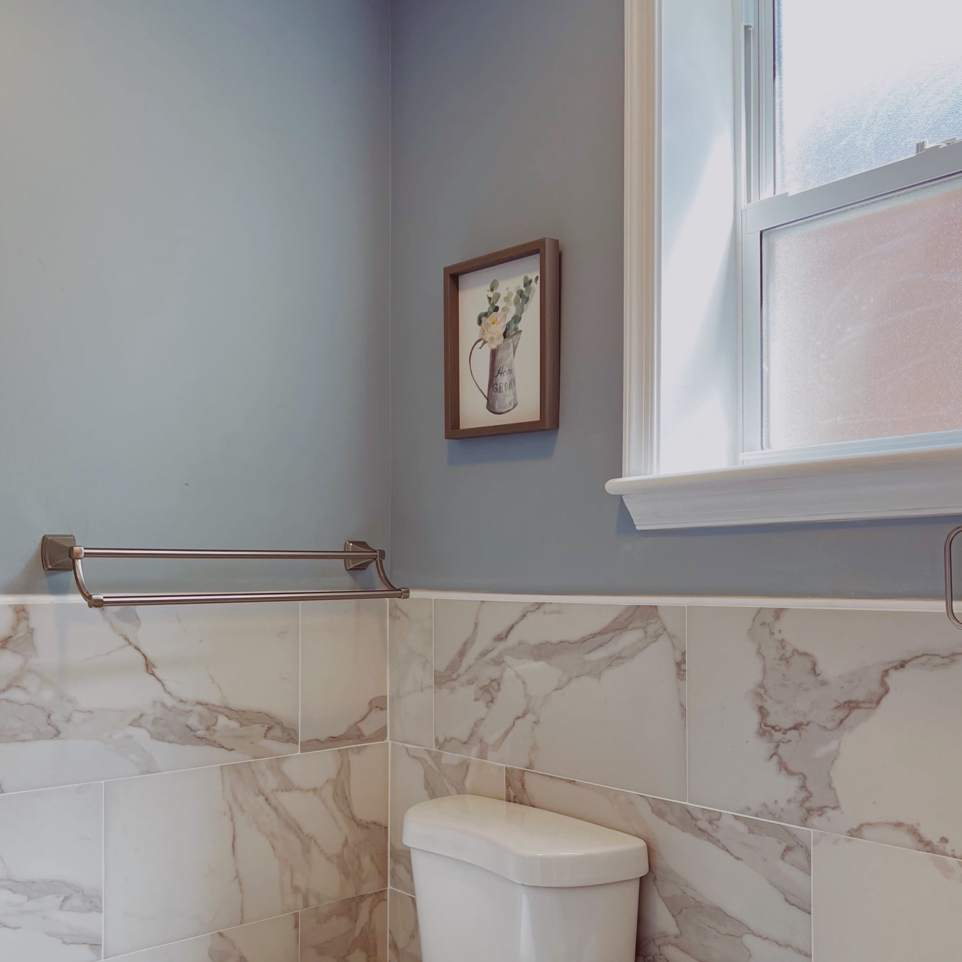 A bathroom with a white toilet, marble-patterned walls, and a framed picture of a vase with flowers on the wall above.