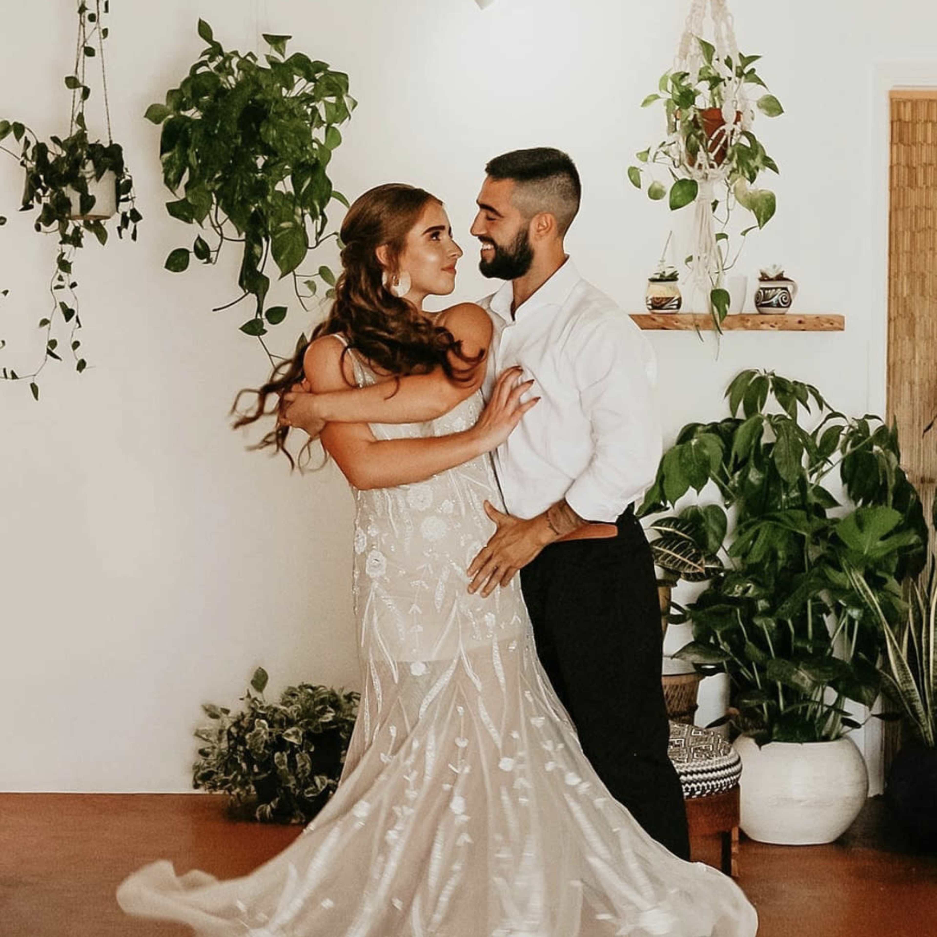 A couple dances together in a brightly lit room adorned with various potted plants.