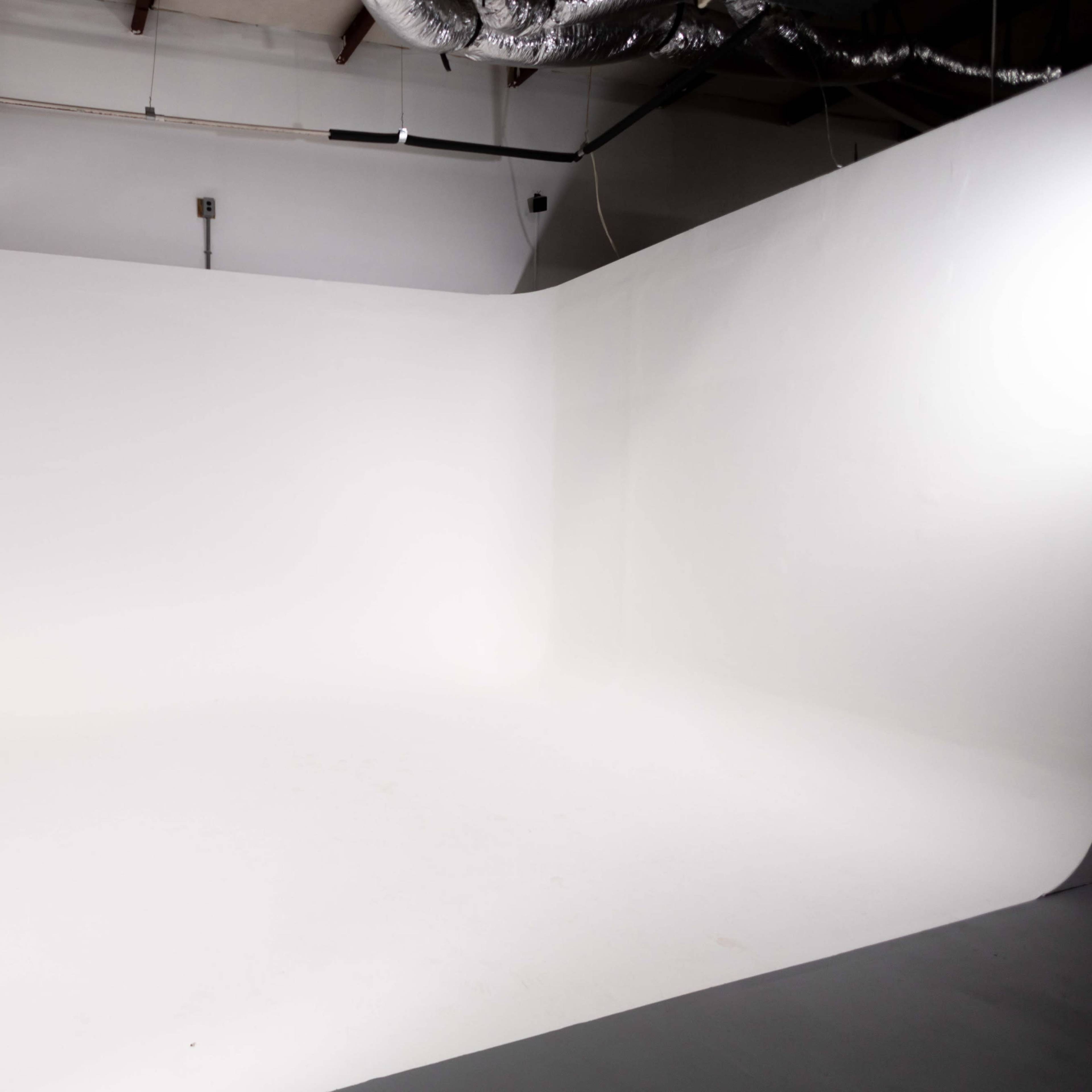 A spacious white photography studio with a seamless backdrop and polished floor.