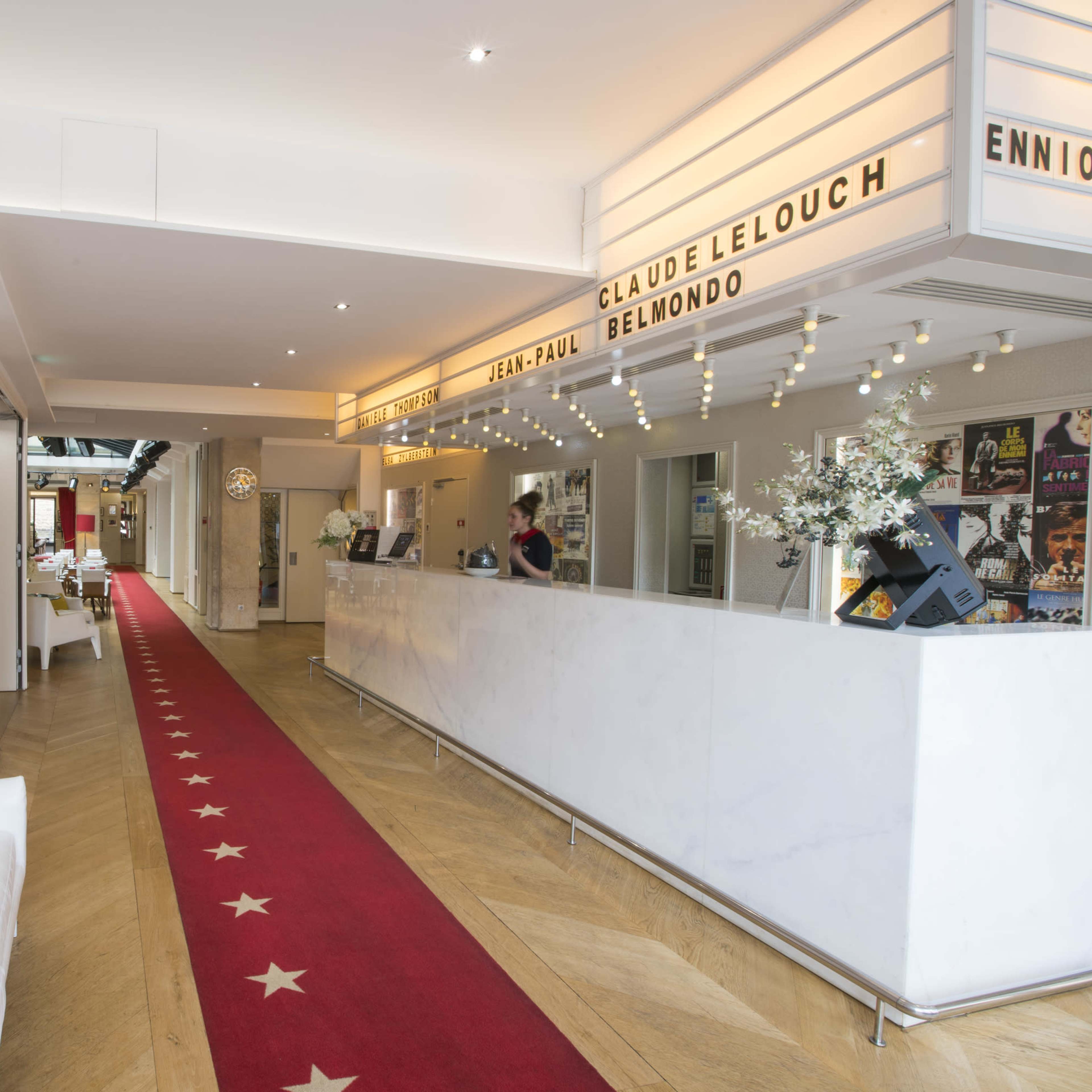 A brightly lit hallway with red carpet and white walls, leading to a reception area adorned with movie-related posters and text displays.