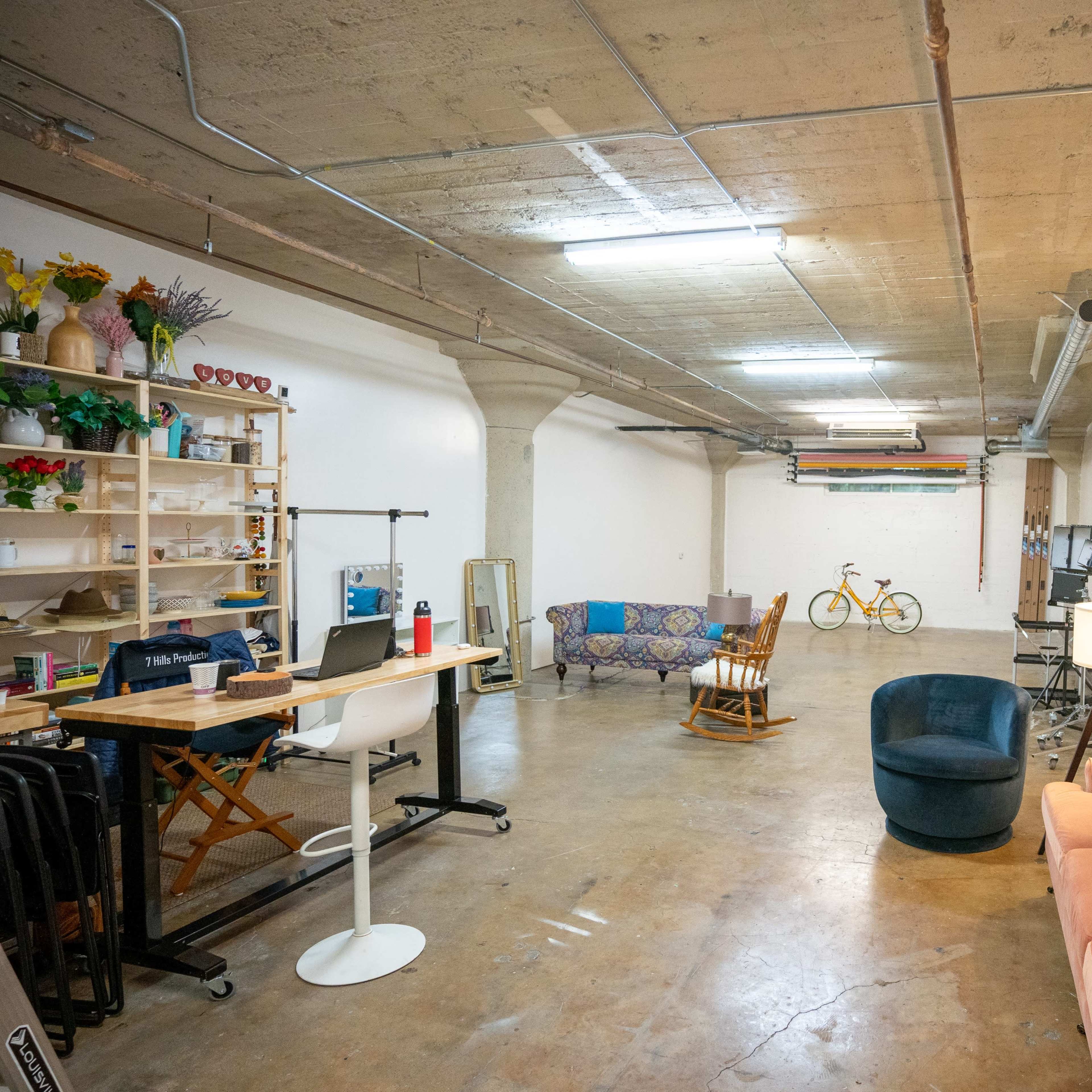 A spacious, well-lit room with a combination of seating areas, a desk workspace, and a bicycle in the background.