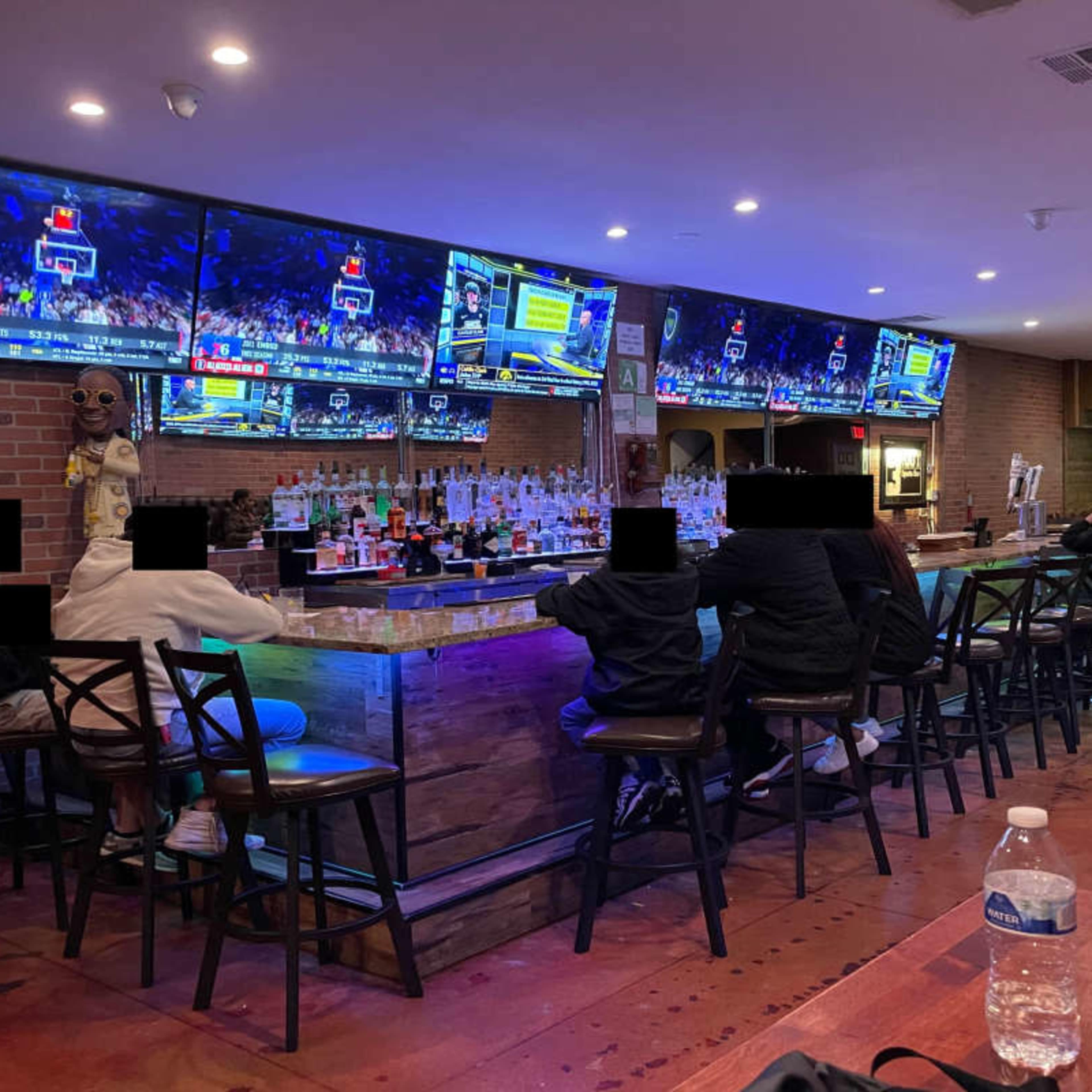 A group of people sit at a bar while multiple screens display a basketball game.