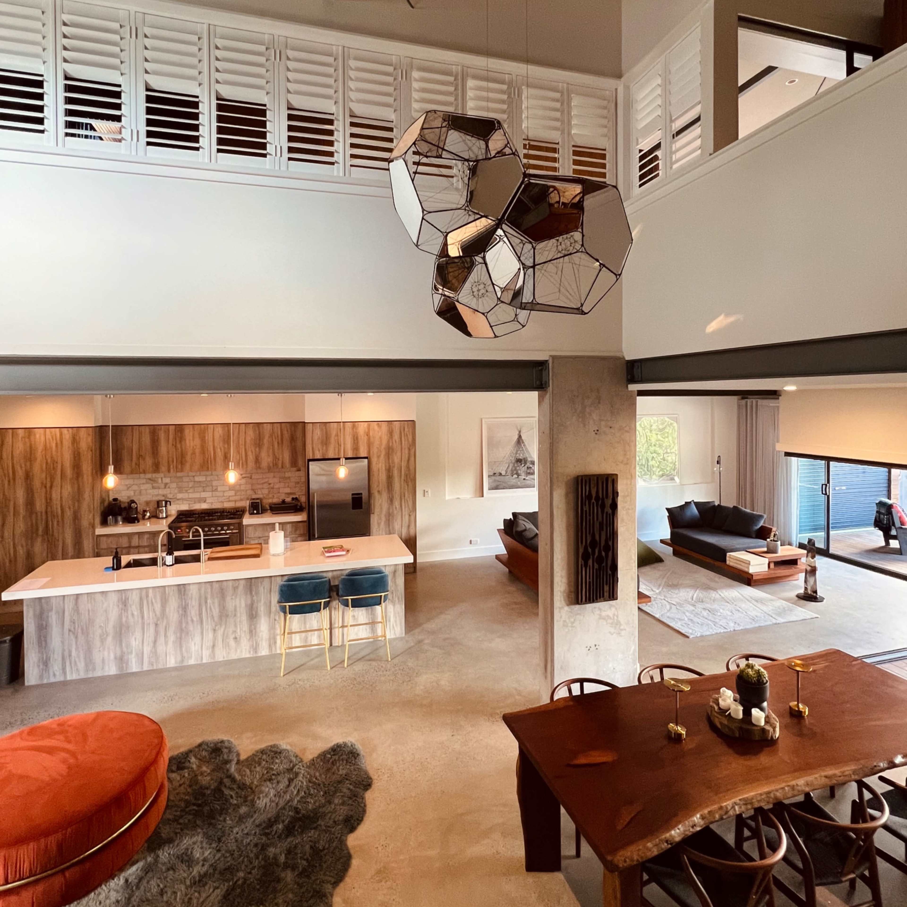 A modern open-concept living space with a kitchen, dining area, and lounge, featuring geometric light fixtures and a mix of textures in the furnishings.