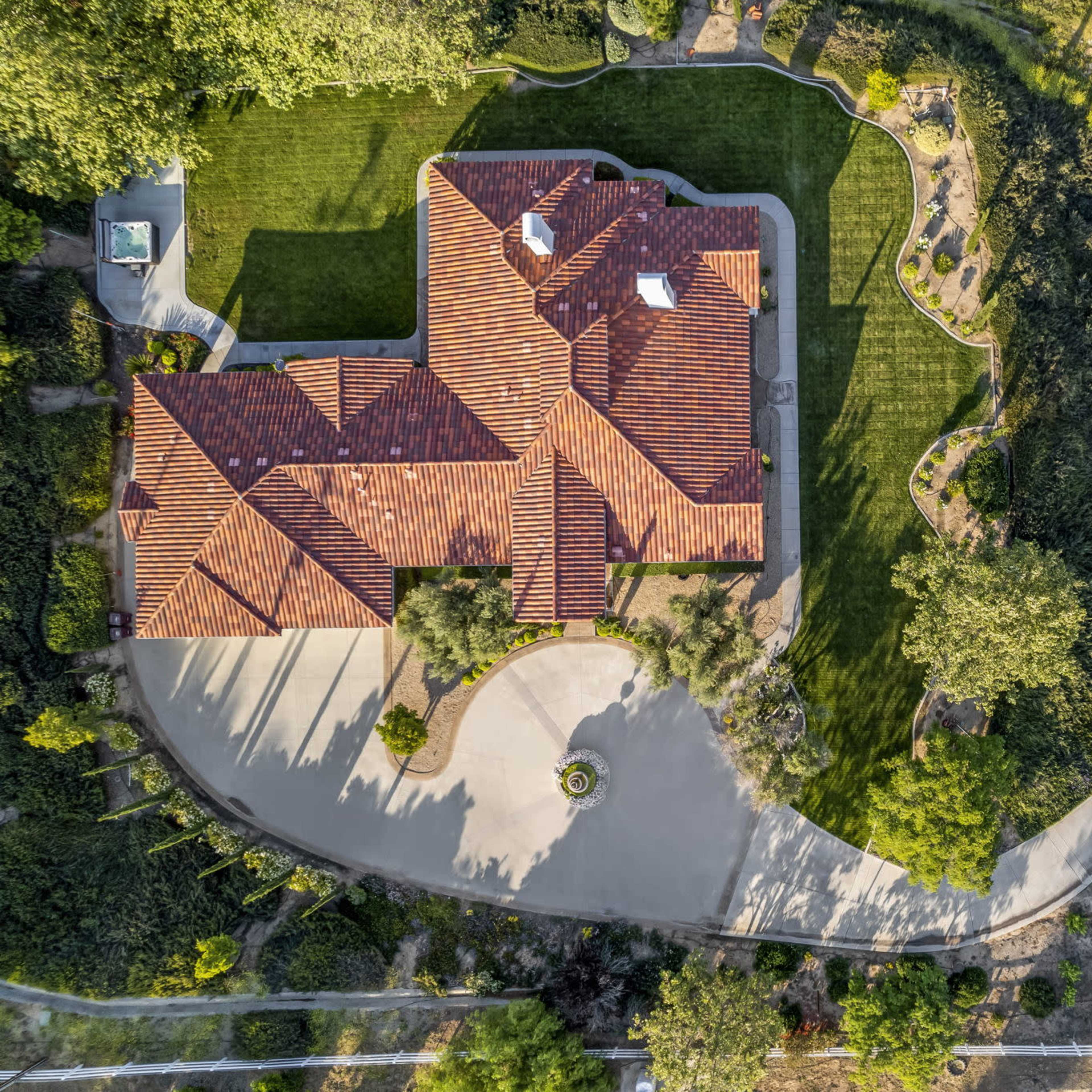 An aerial view of a large residential property featuring a house with a red tiled roof, manicured lawns, and a winding driveway.