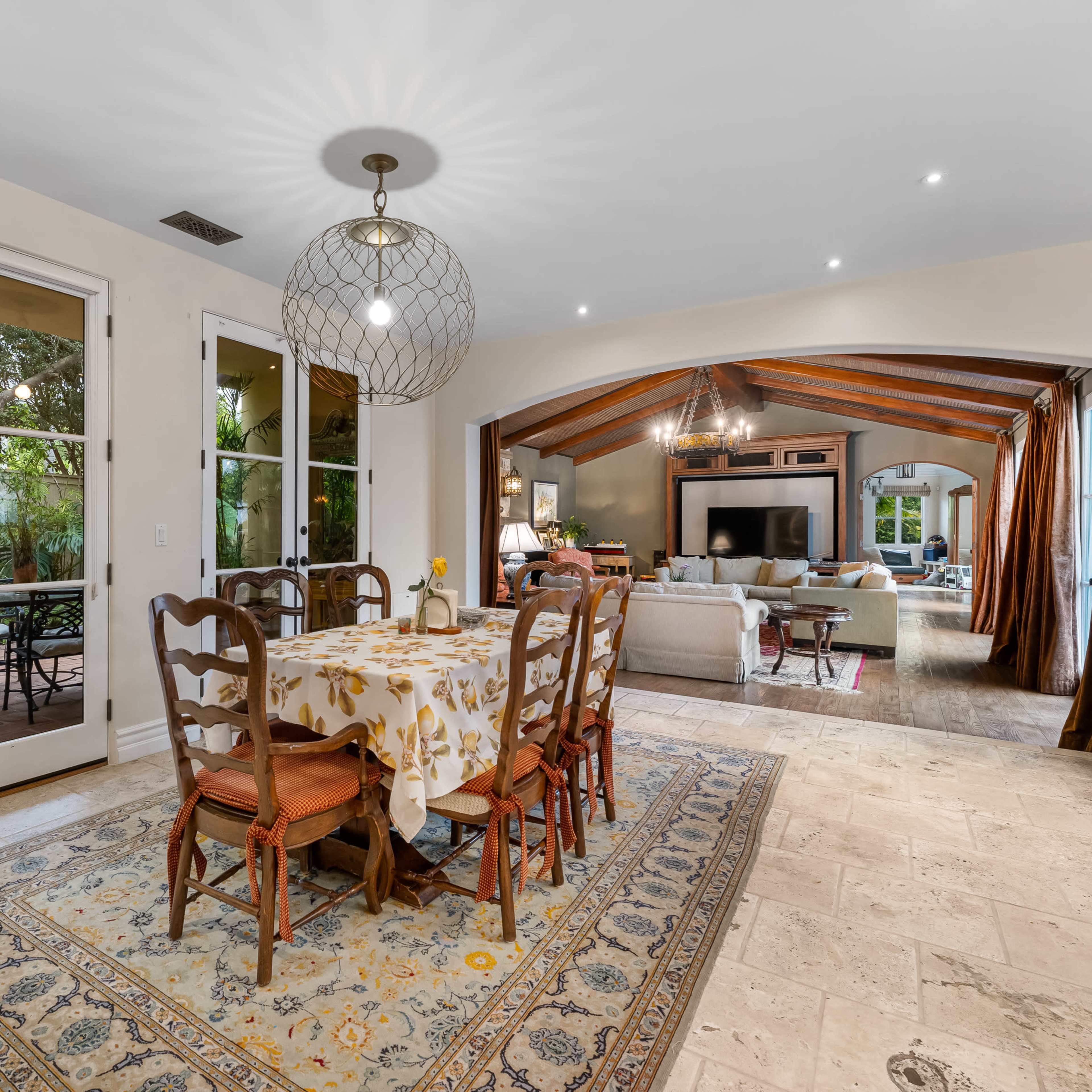 A dining area features a table surrounded by chairs, with doors leading to an outdoor patio and a view of an adjacent living space.