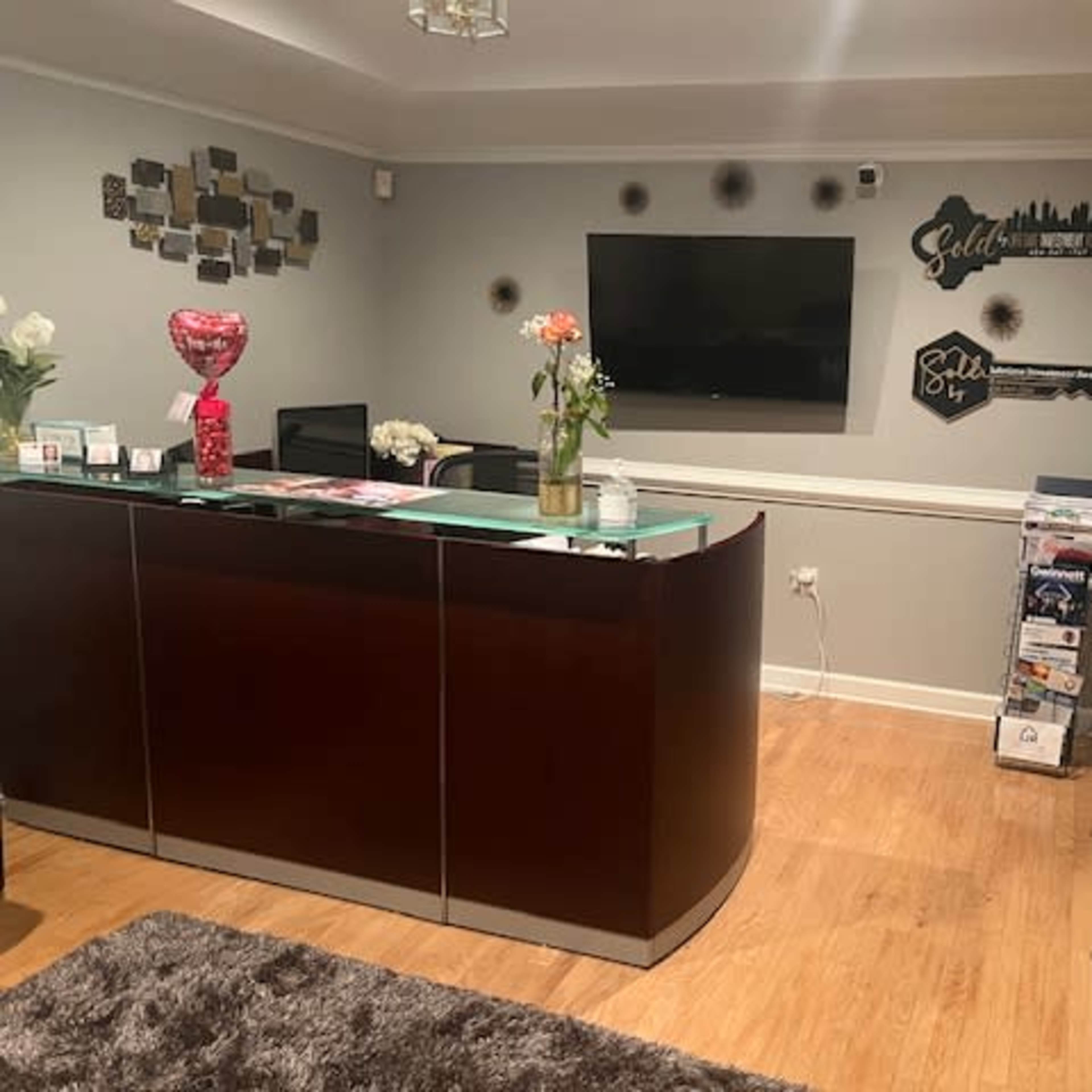 A reception area with a curved wooden desk, a television mounted on the wall, and decorative elements including a guitar silhouette and various magazines displayed on a stand.