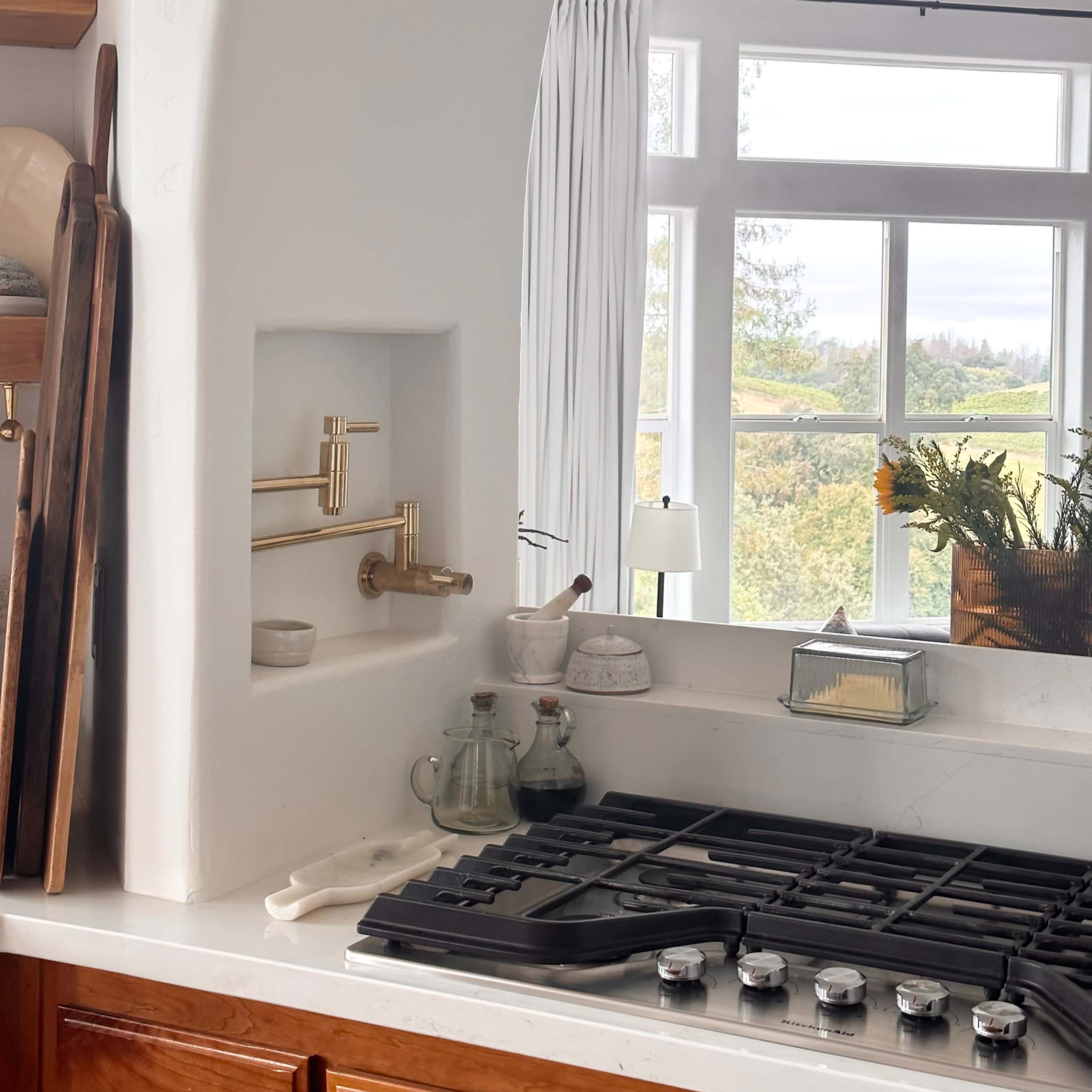 A bright kitchen with a white archway, a gas stove, and a view of greenery through large windows.