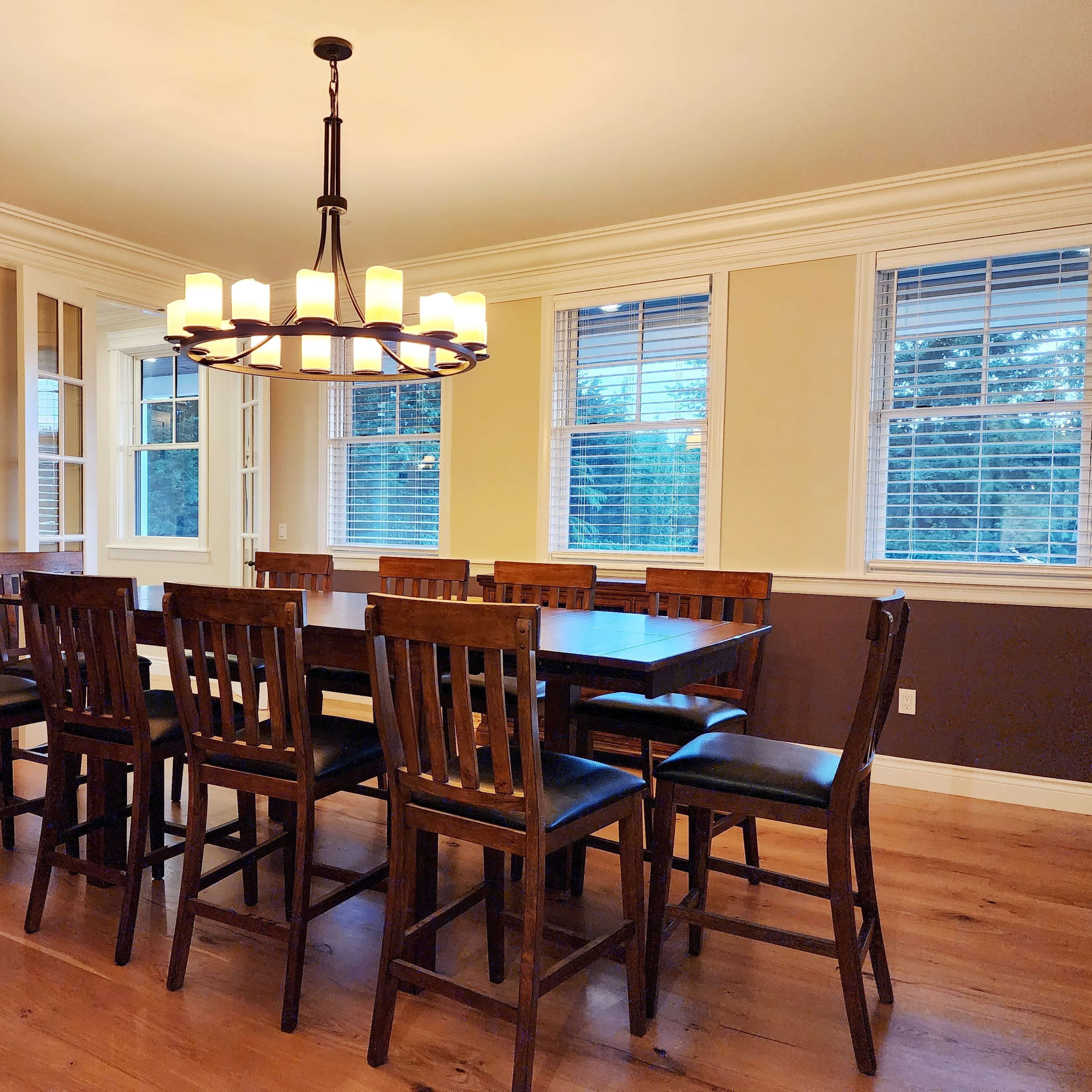 A spacious dining room features a large wooden table surrounded by high-backed chairs and a decorative chandelier overhead.