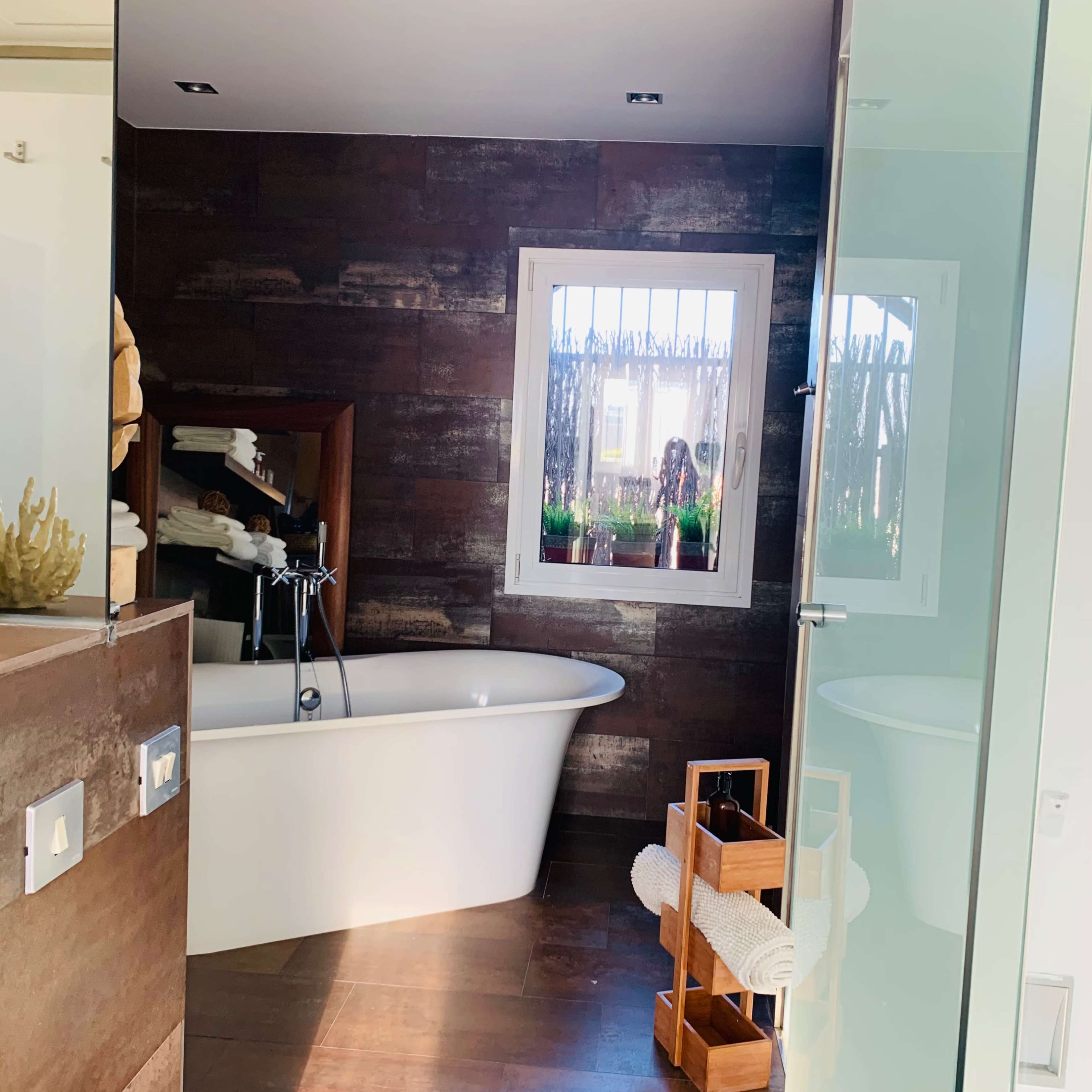 A modern bathroom featuring a freestanding bathtub, a wooden accent wall, and a glass shower enclosure.
