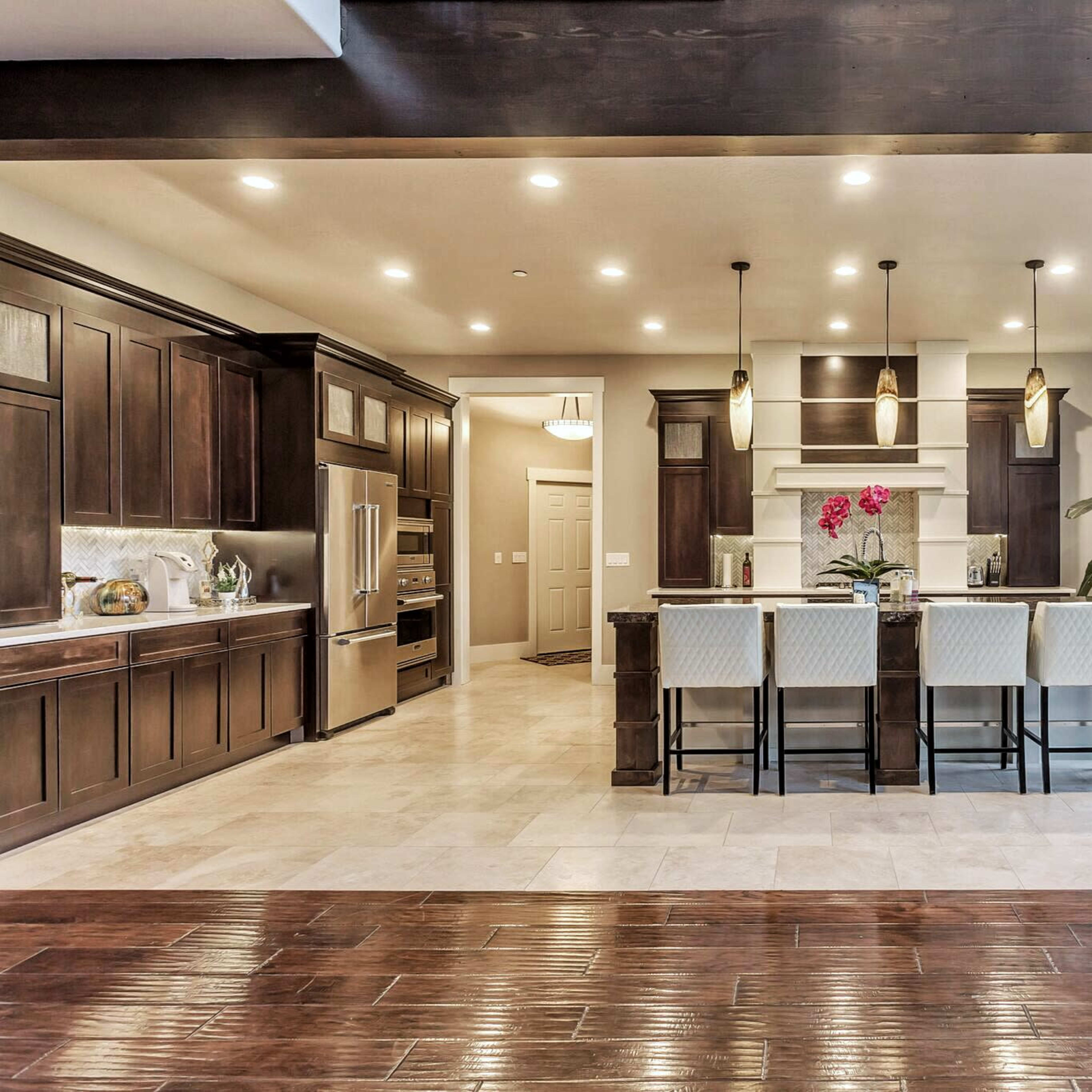 A modern kitchen features dark wooden cabinetry, a large central island with seating, and bright lighting.