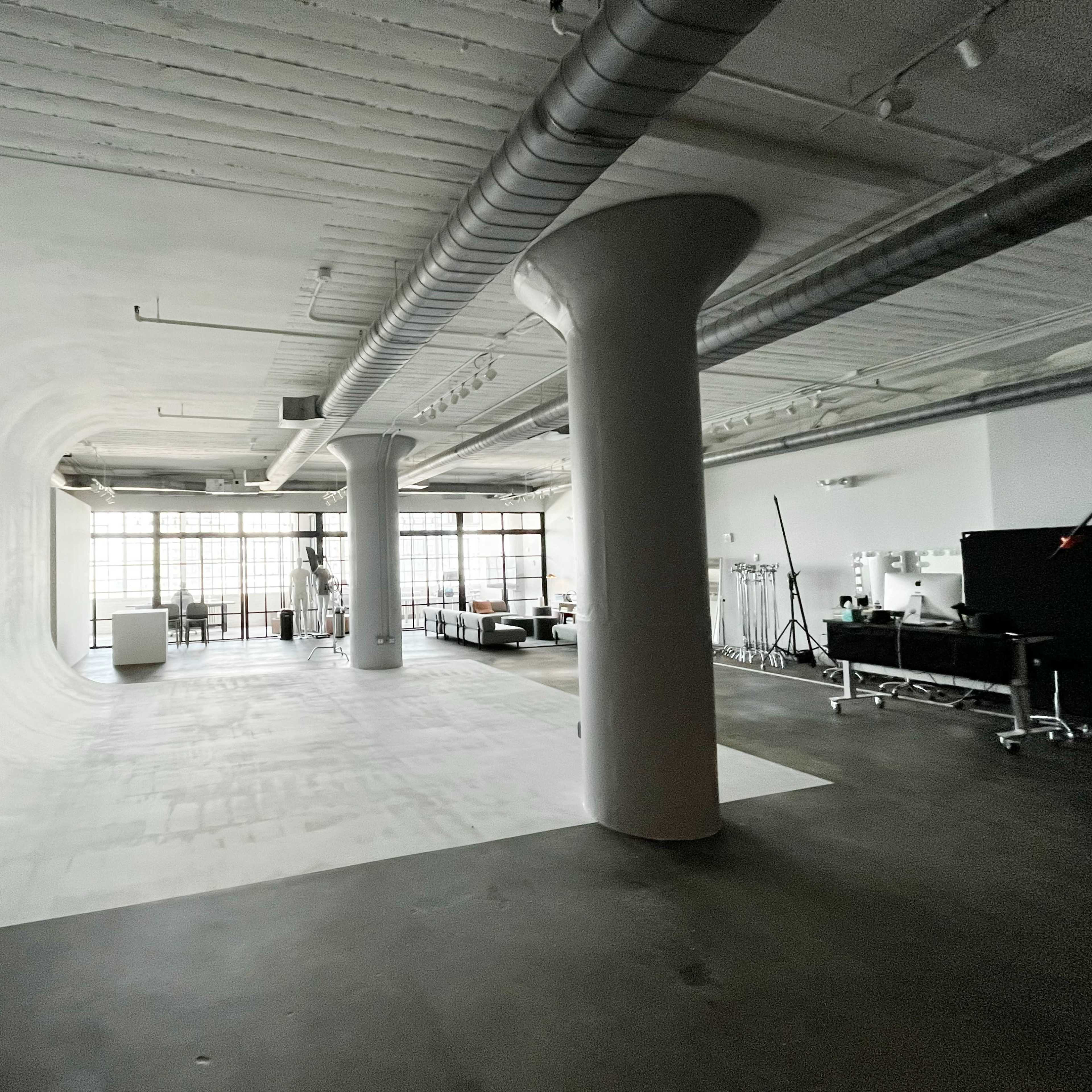 A spacious studio with a smooth, curved white backdrop, large windows allowing natural light, and various pieces of furniture and equipment.