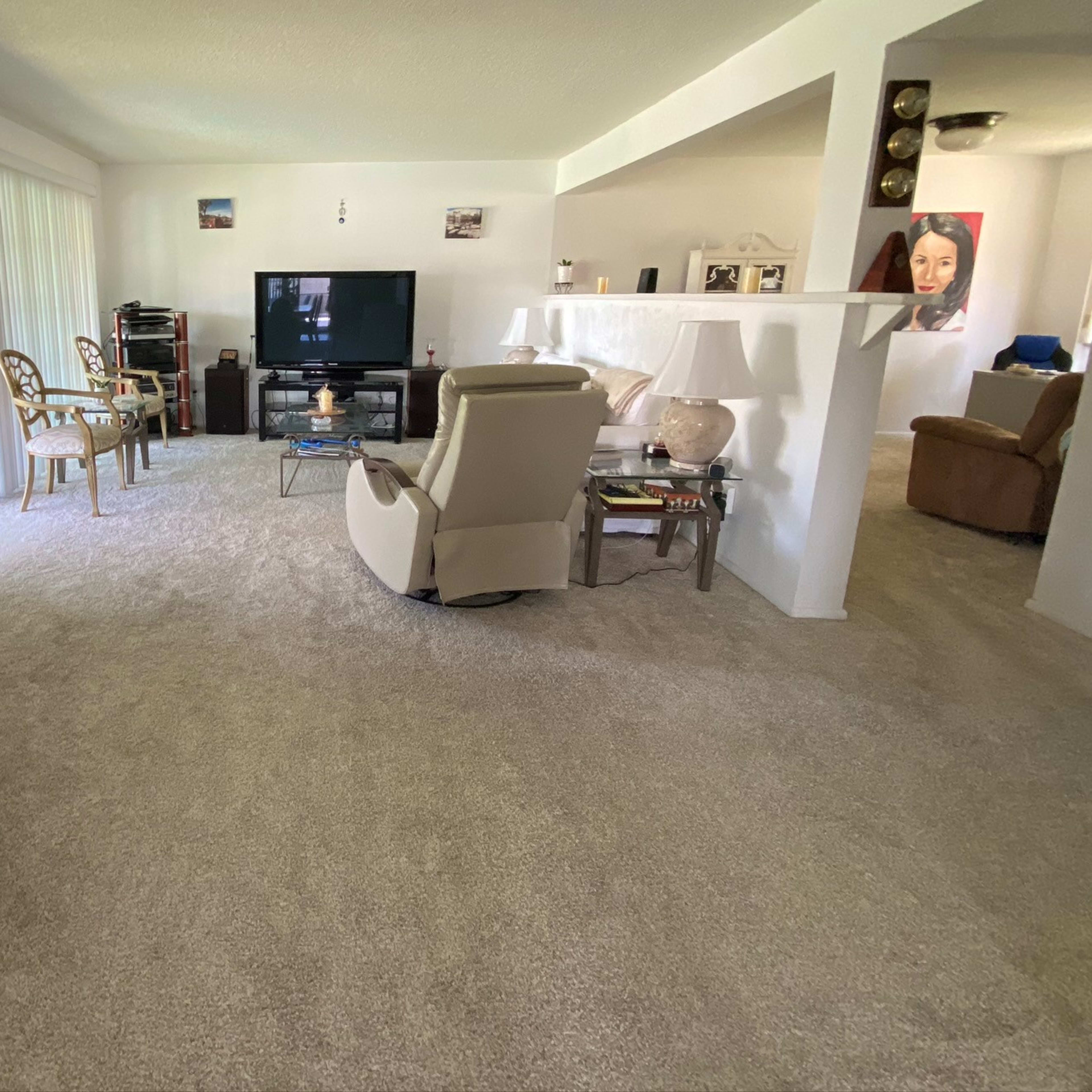 A spacious living room with a fireplace, a television, various seating options, and soft carpeting.