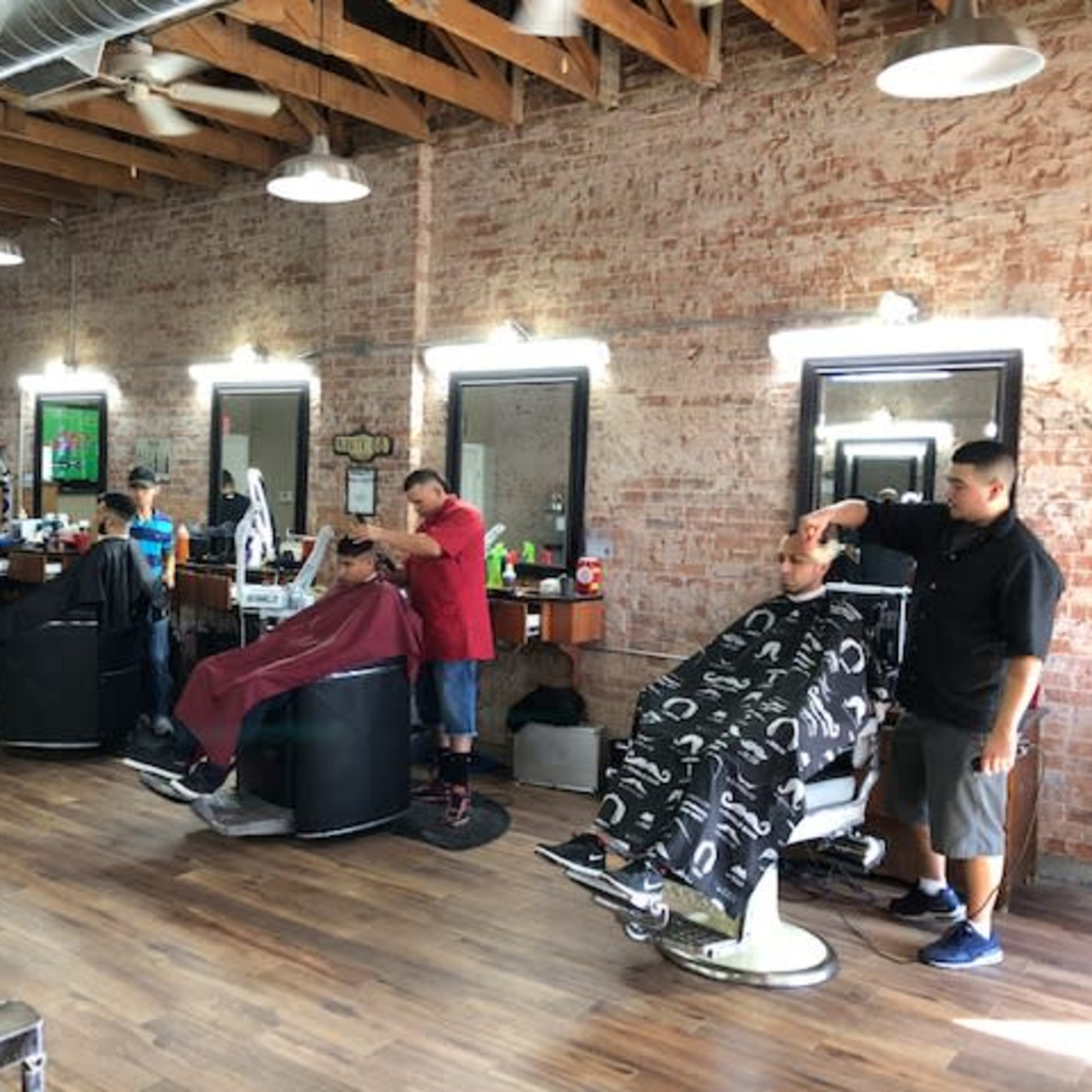 A barbershop with several clients getting haircuts, while barbers work at their stations along a brick wall.