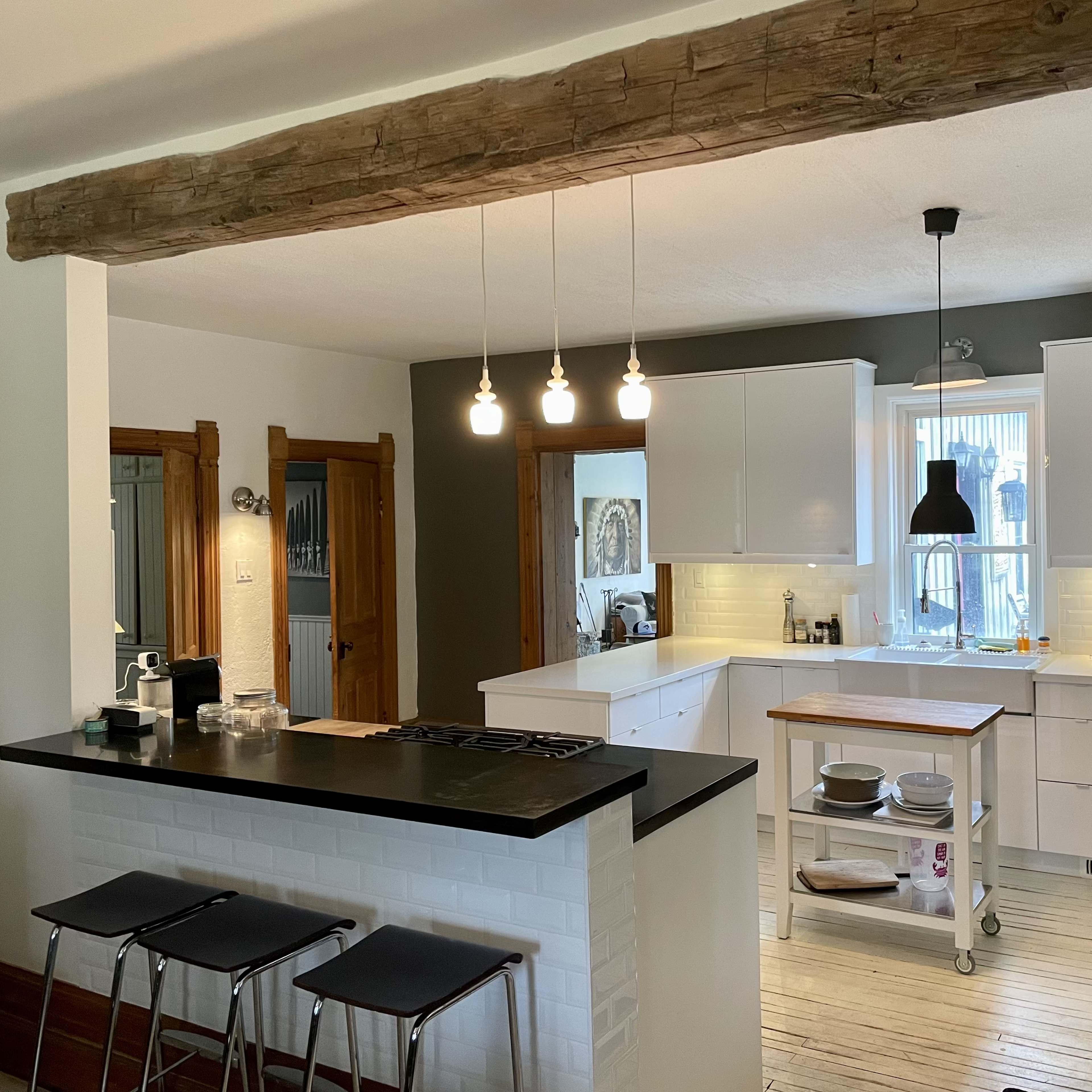 A modern kitchen features white cabinetry, a wooden beam overhead, and a central island with bar stools.