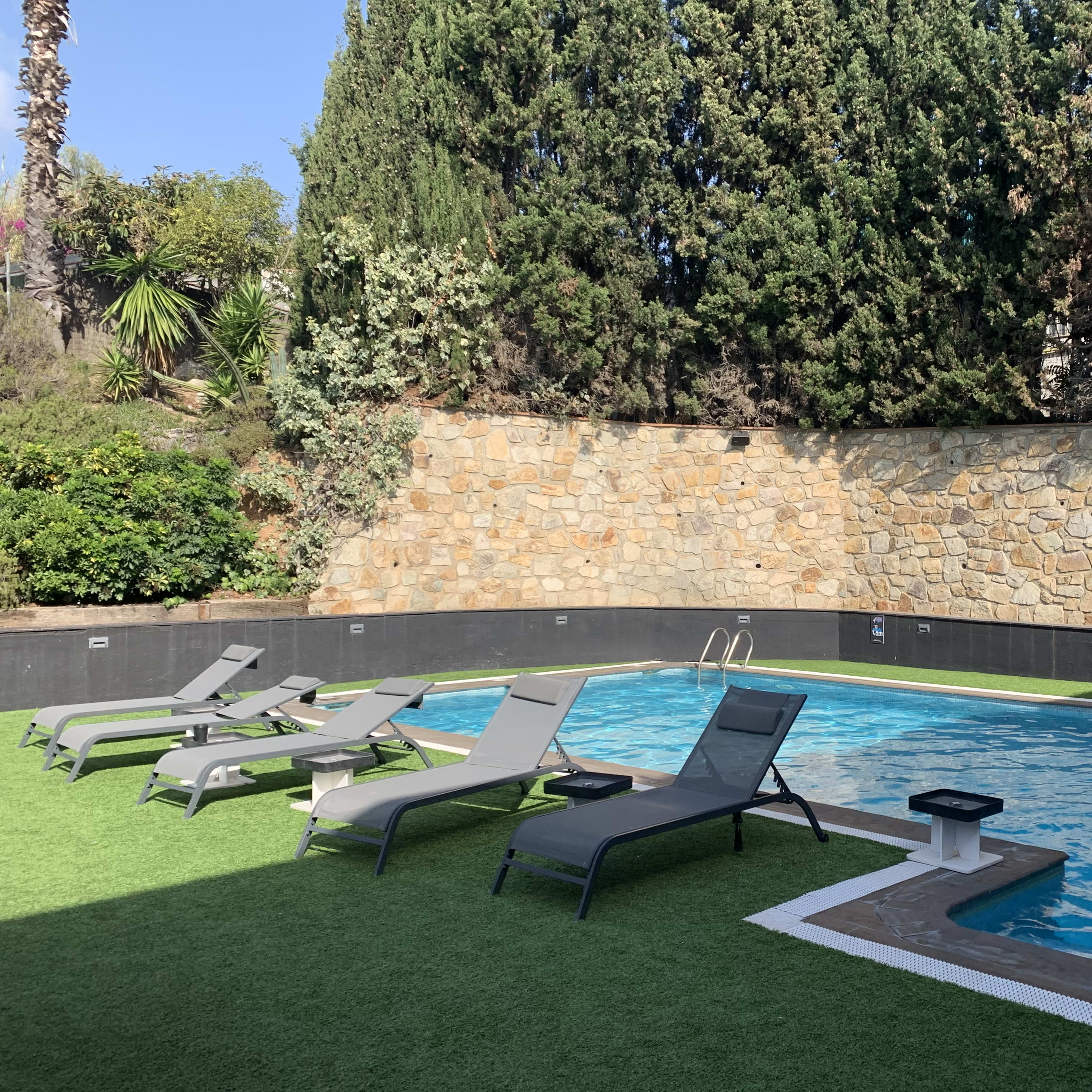 A swimming pool surrounded by lounge chairs on a grassy area, enclosed by a stone wall and greenery.