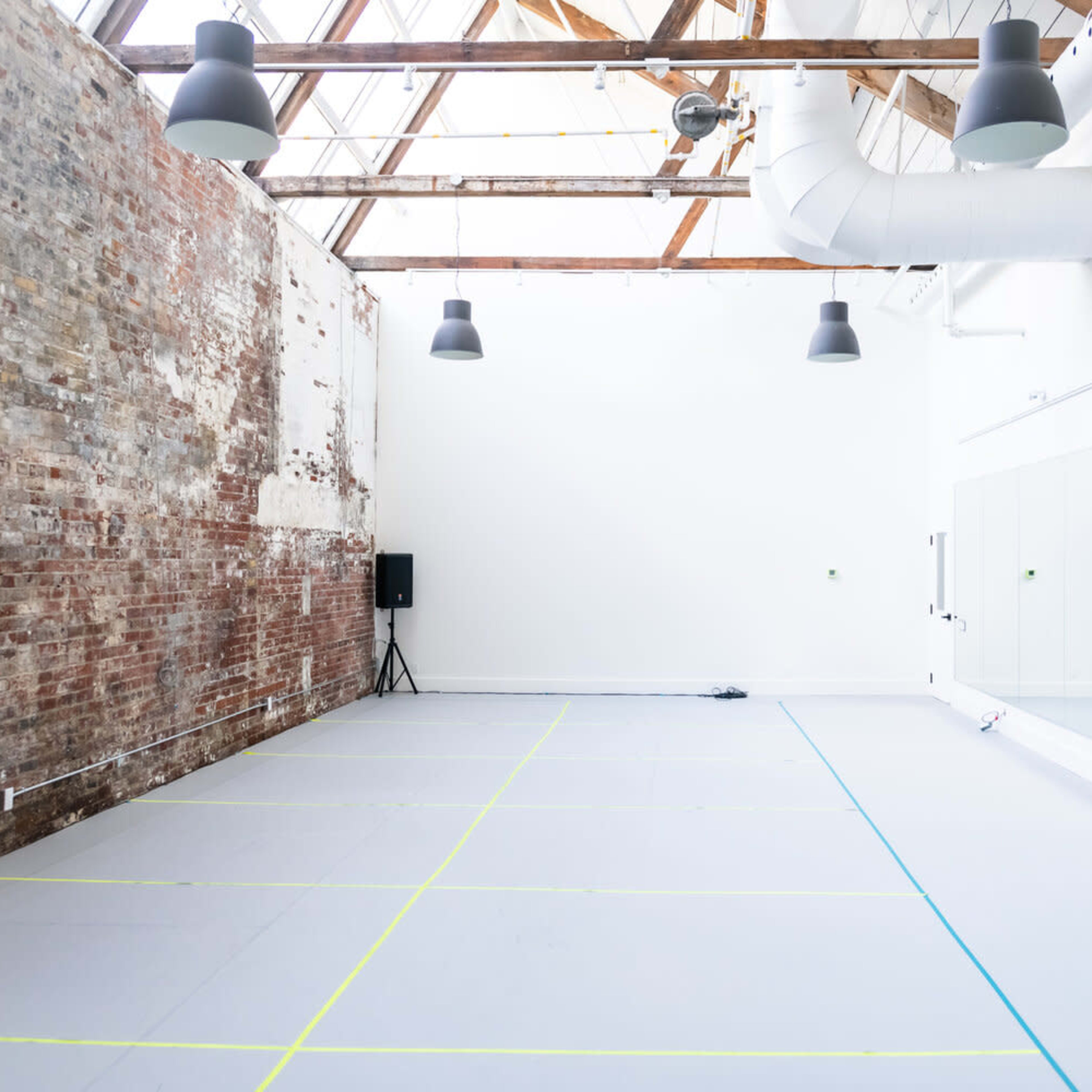 A spacious dance studio with exposed brick walls, a mirrored wall, and a gray floor marked with blue and yellow lines.