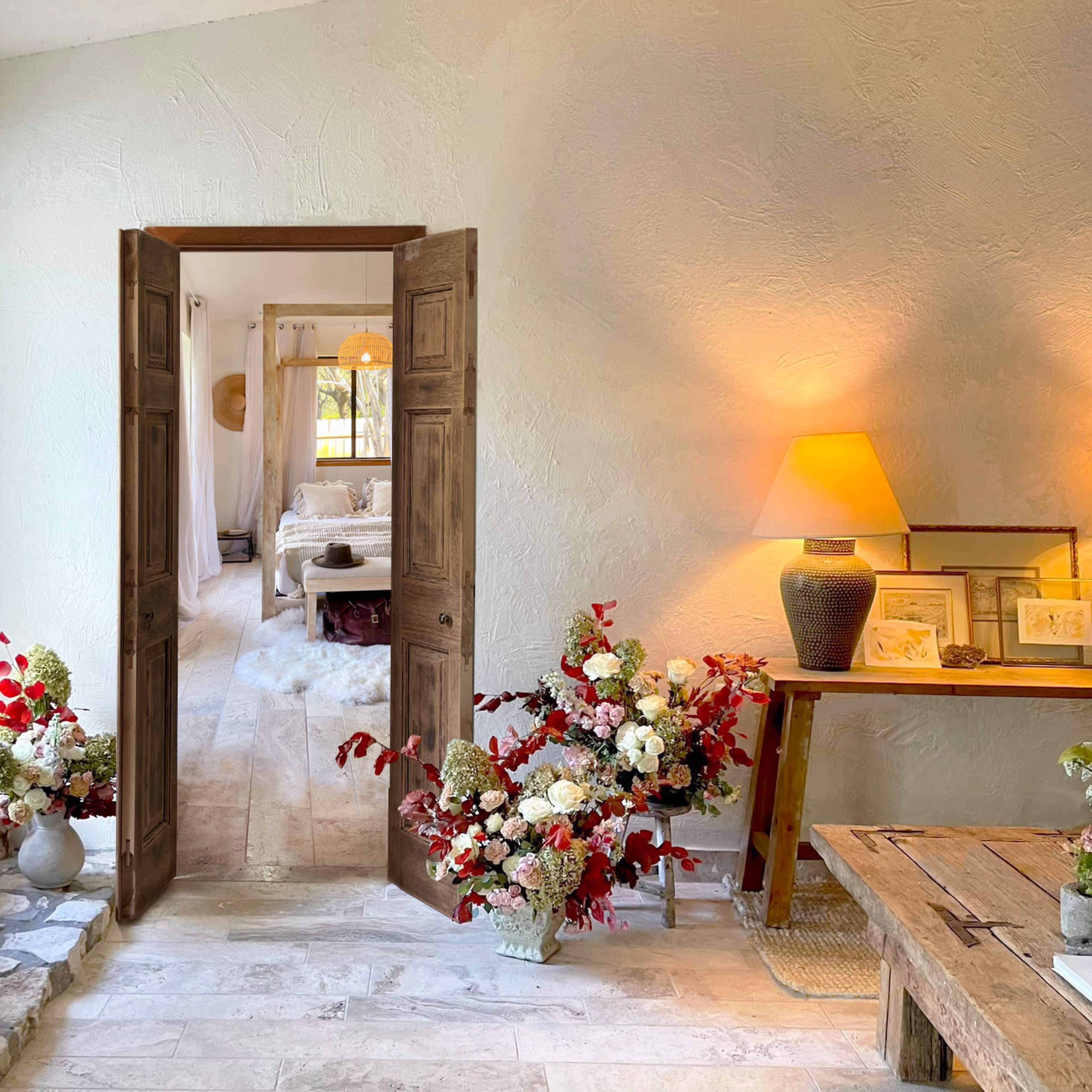 A welcoming entrance features a set of open double doors leading to a cozy room, with a table adorned with flowers and two lamps casting a warm glow.