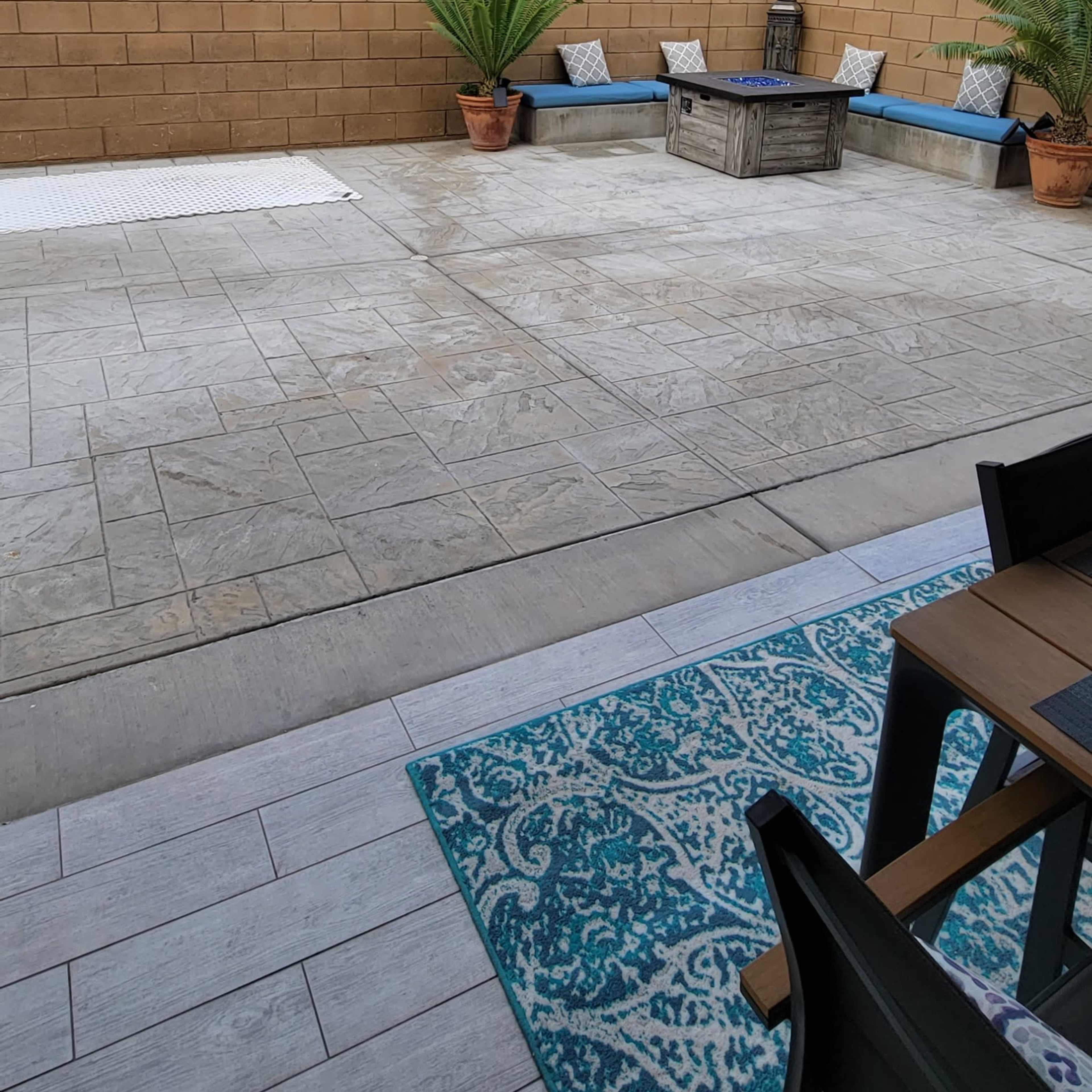 A landscaped patio area with a concrete floor, potted plants, and a decorative wall, with string lights overhead and a seating arrangement visible.
