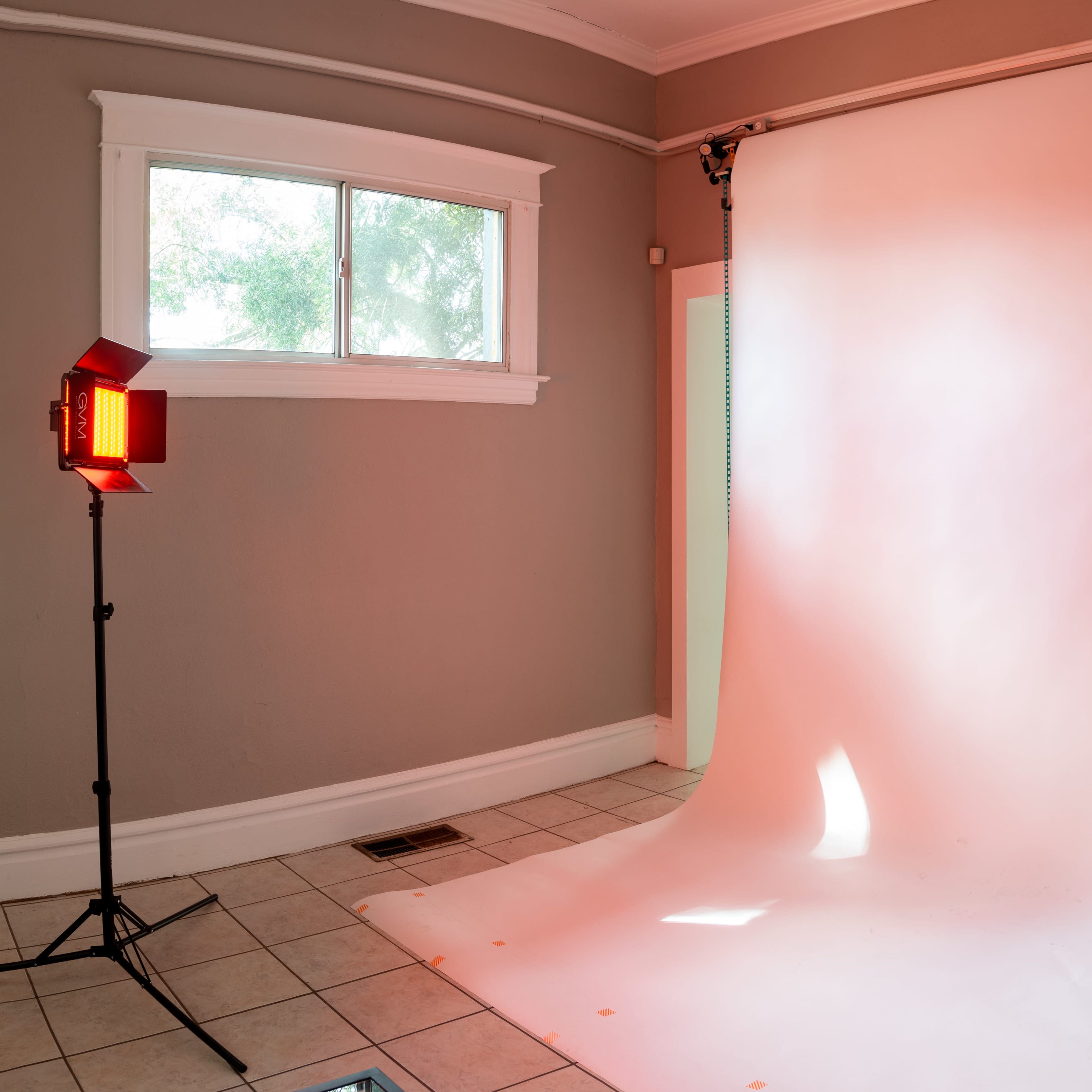 A photography studio setup with a roll of white backdrop, a window, and a lighting device positioned nearby.