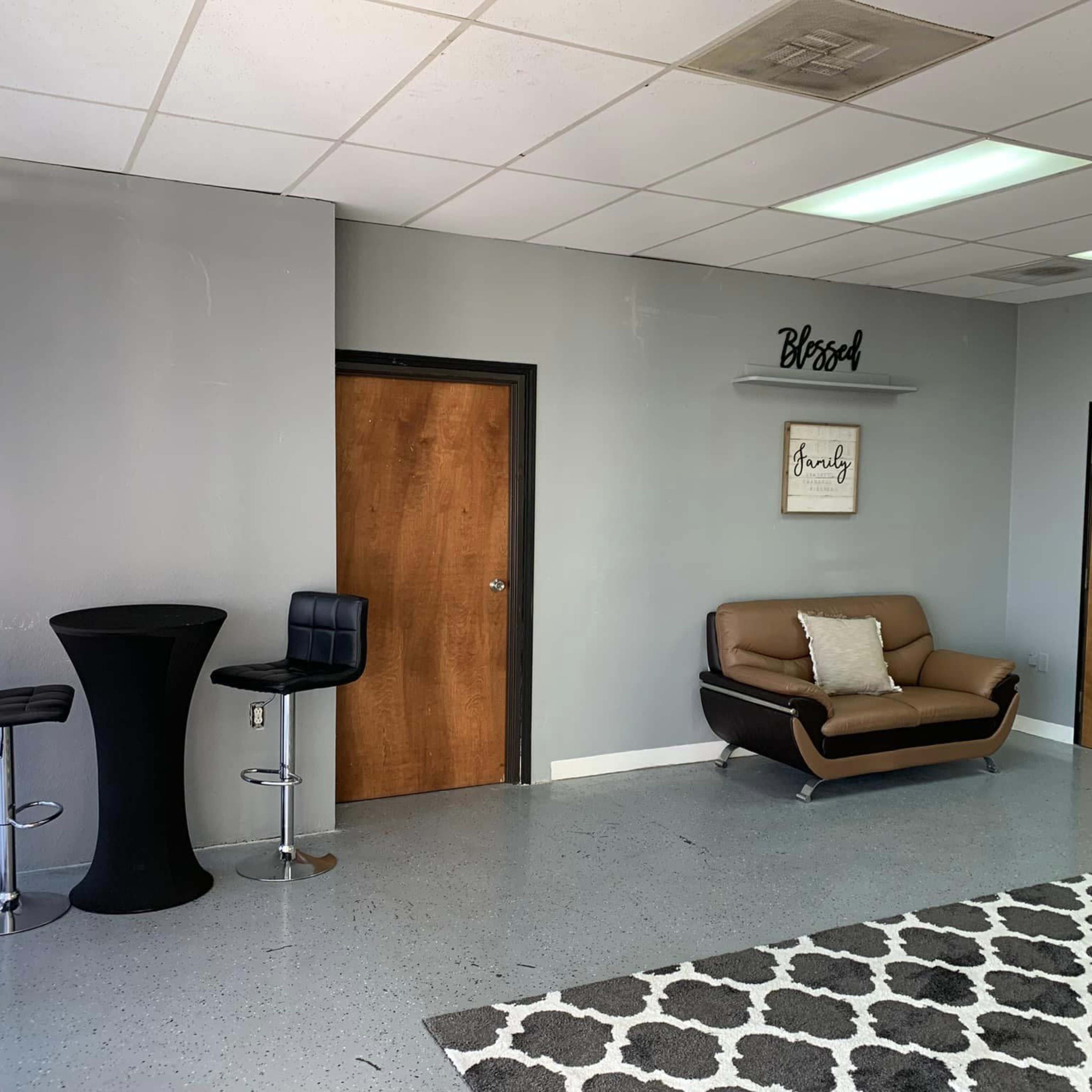 A minimalist interior space with a sofa, two tall tables, and a decorative wall sign that reads "Blessed."