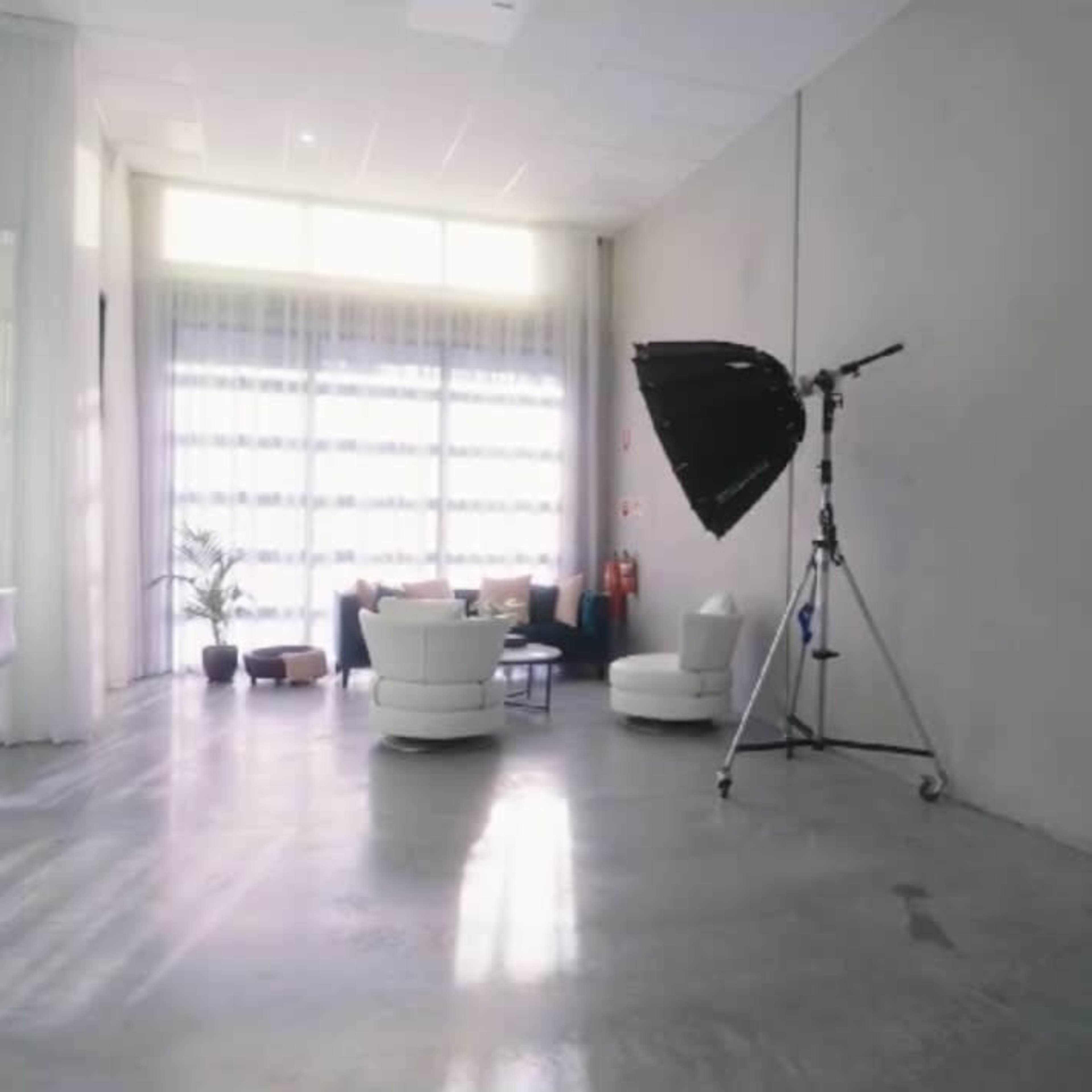A minimalistic studio space featuring a makeup vanity with lights, a seating area with a sofa, and a large light stand in the corner.