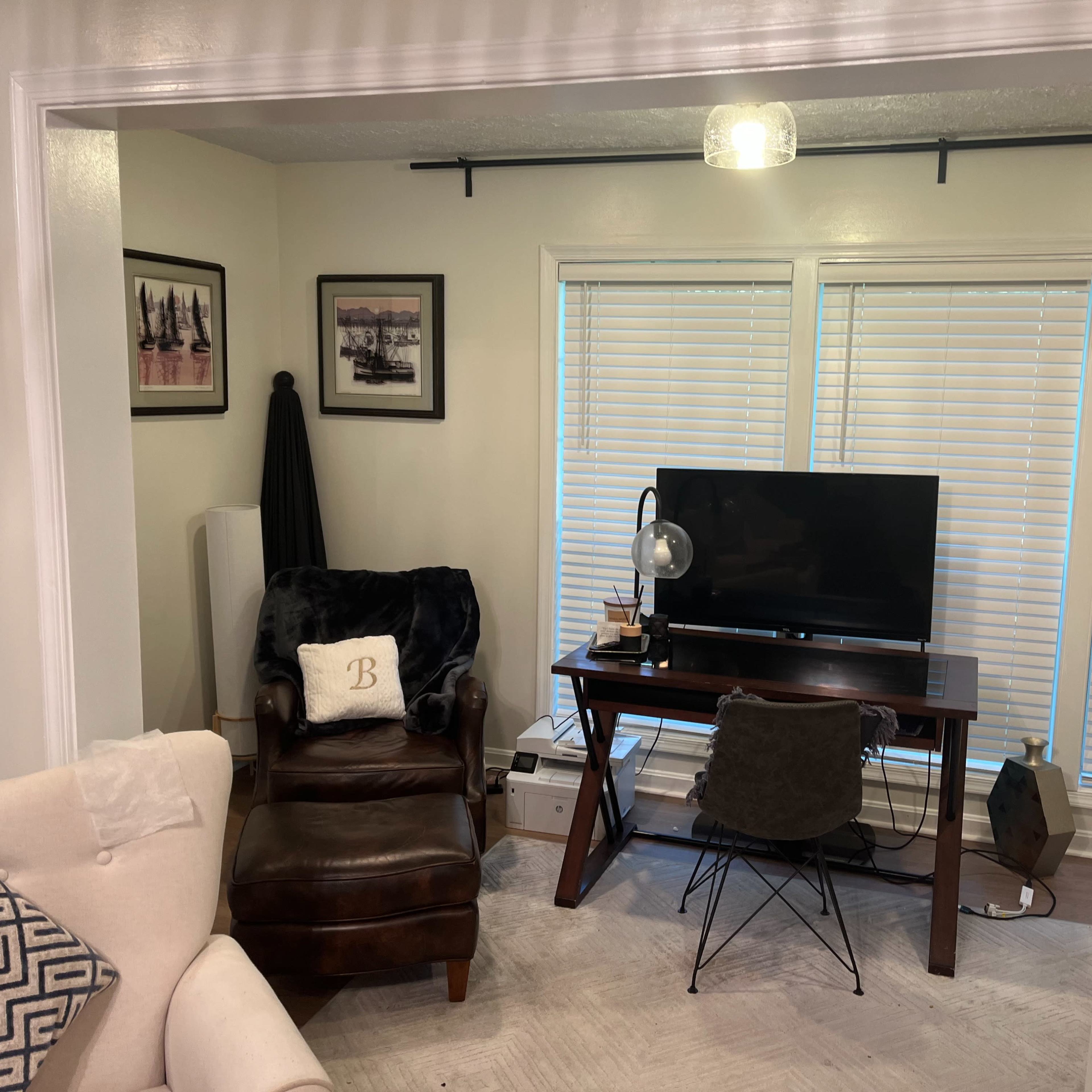 A small home office space with a desk, a television, and a leather chair, illuminated by natural light from a nearby window.
