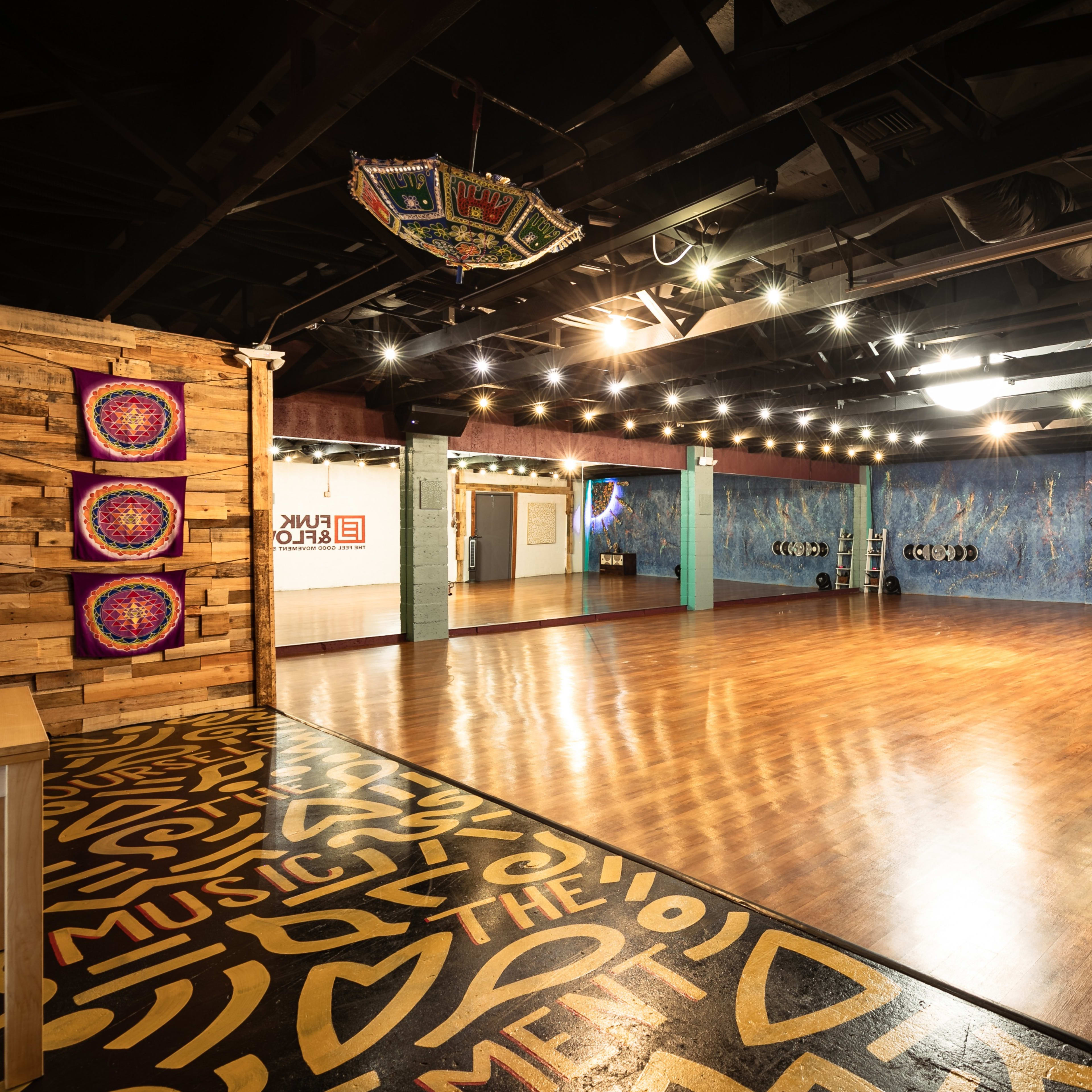 An empty dance studio features polished wooden floors, colorful wall murals, and dim overhead lighting.