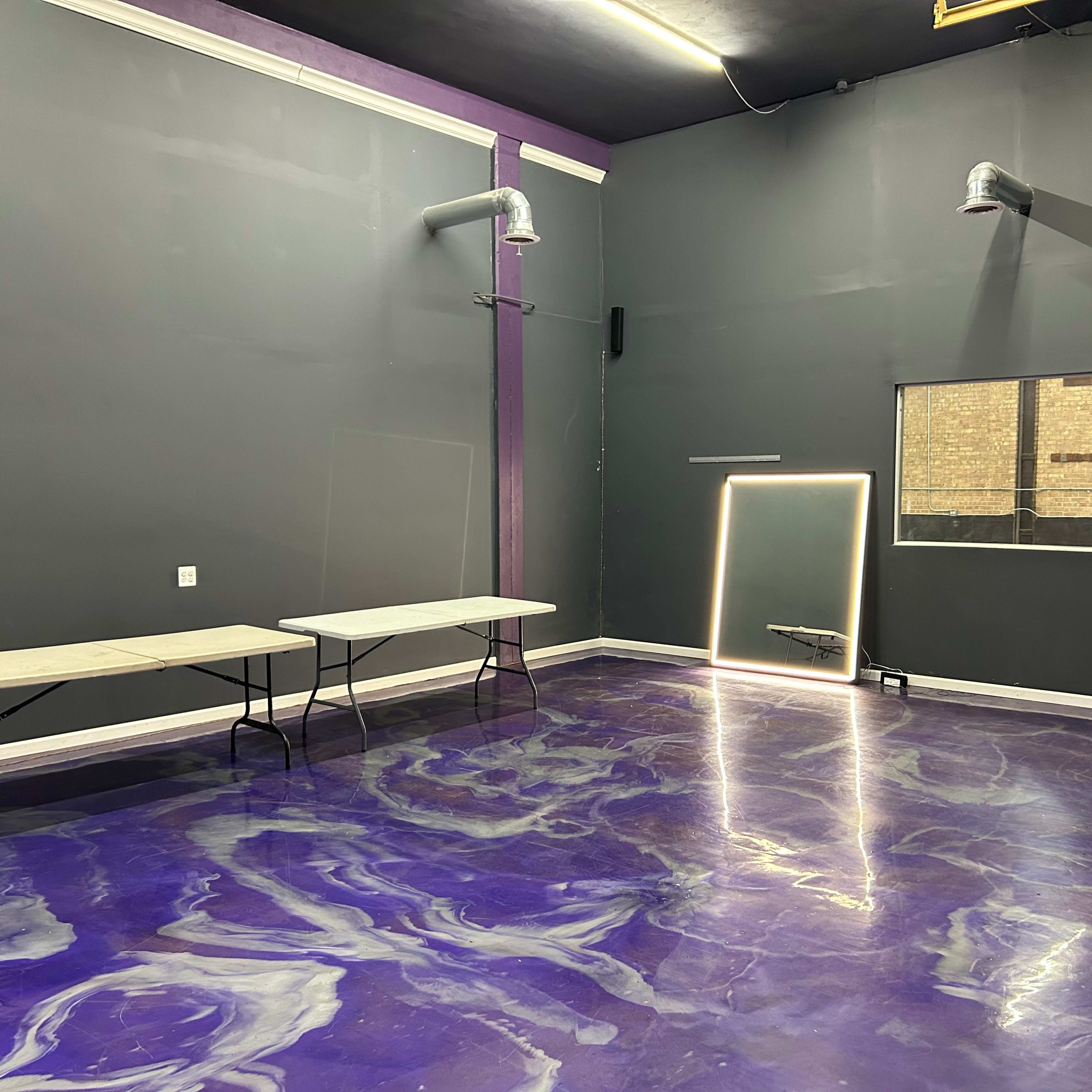 An empty room with purple-painted walls, two folding tables, and a floor featuring a swirling purple design.