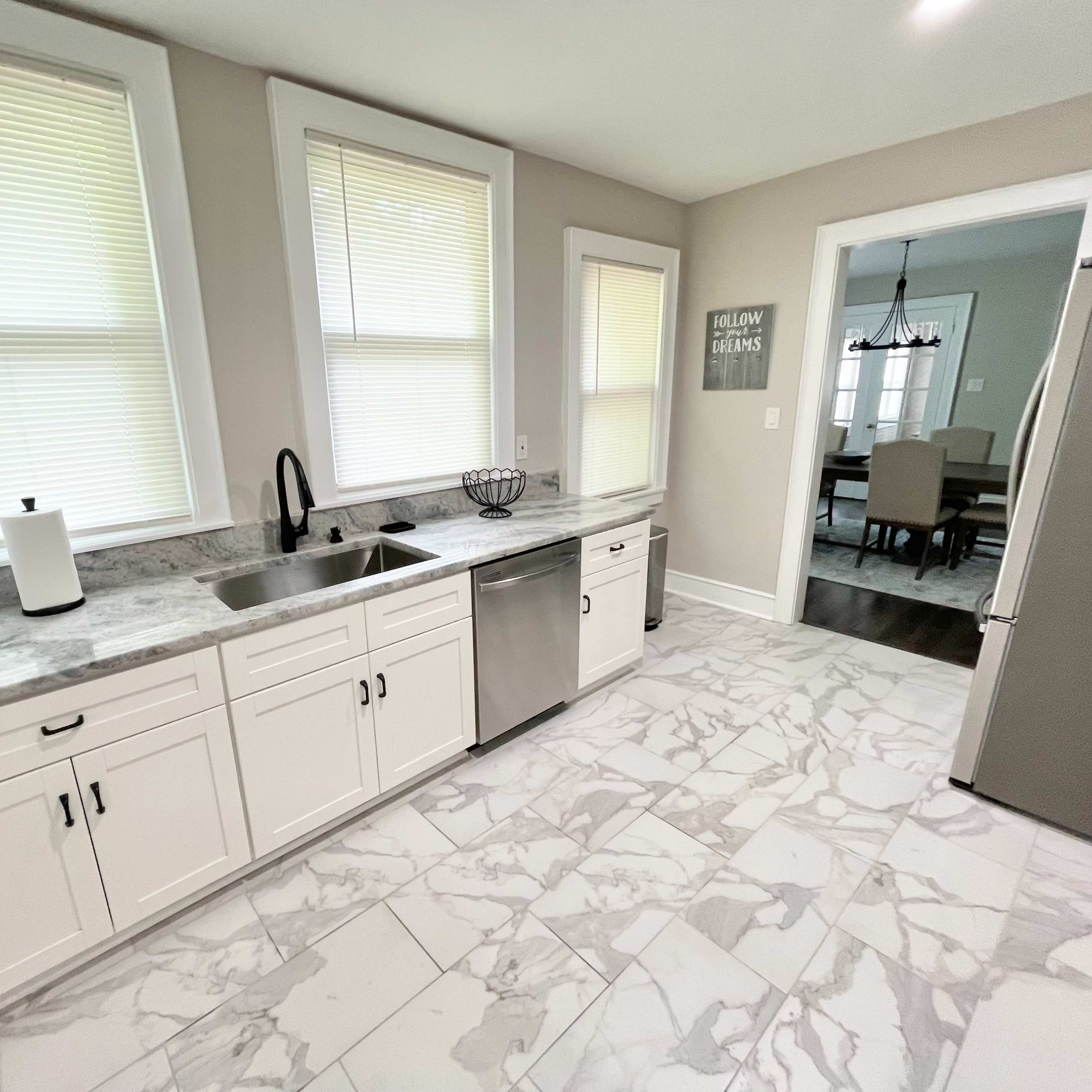 A modern kitchen with white cabinetry, a stainless steel dishwasher, and marble-patterned flooring.
