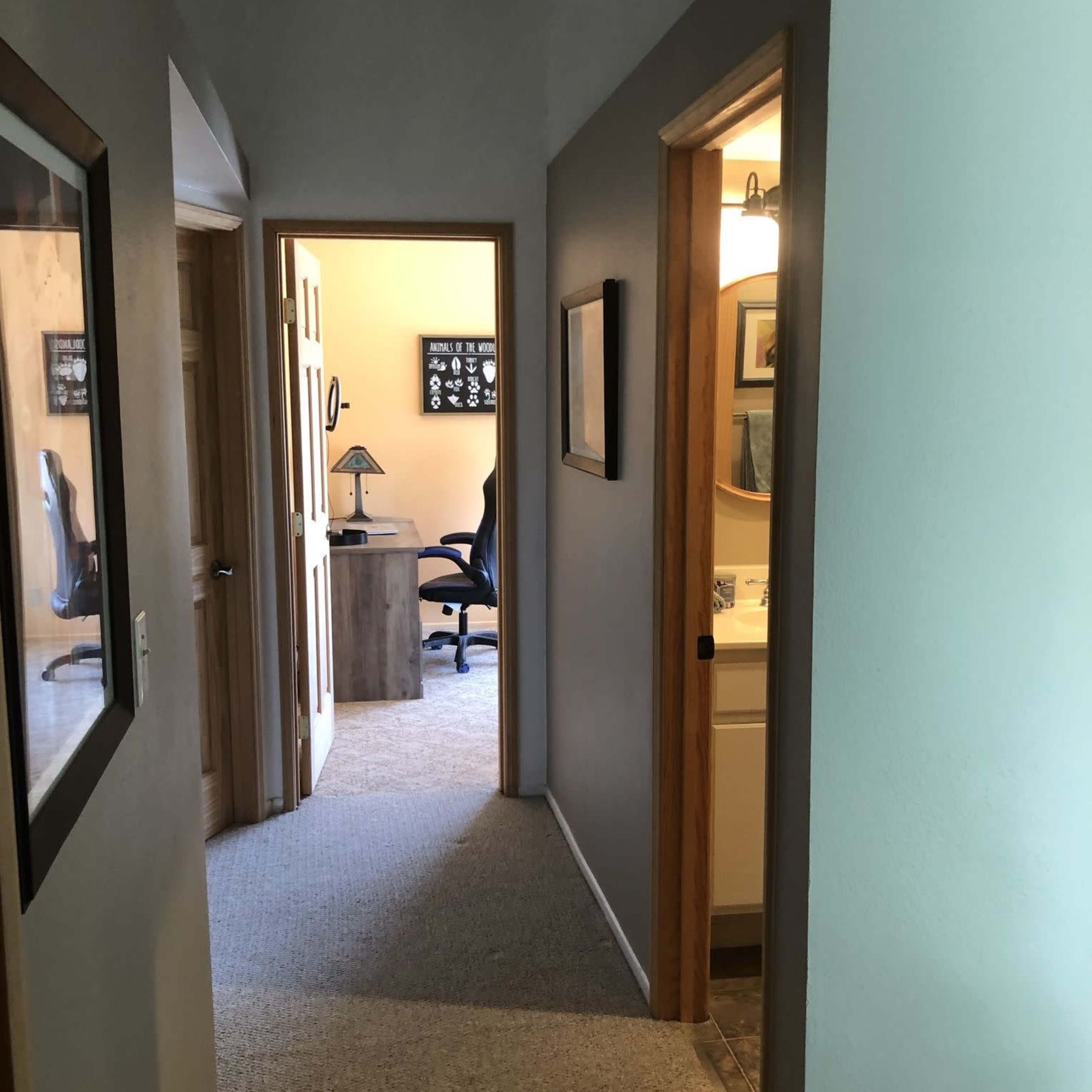 A hallway with doors leading to rooms, including a visible bathroom and an office area.