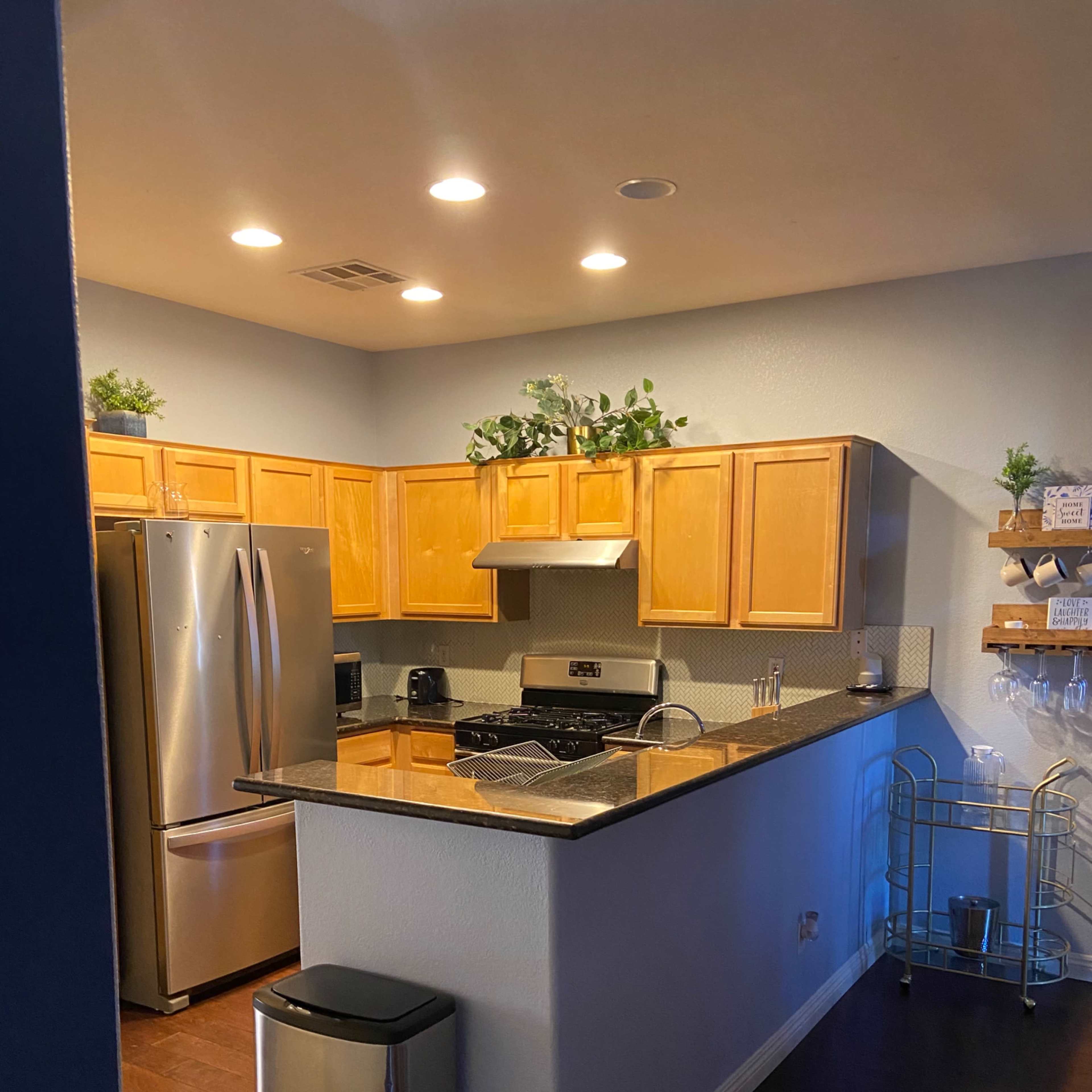 A modern kitchen features wooden cabinets, a stainless steel refrigerator, and a granite countertop with a bar area.