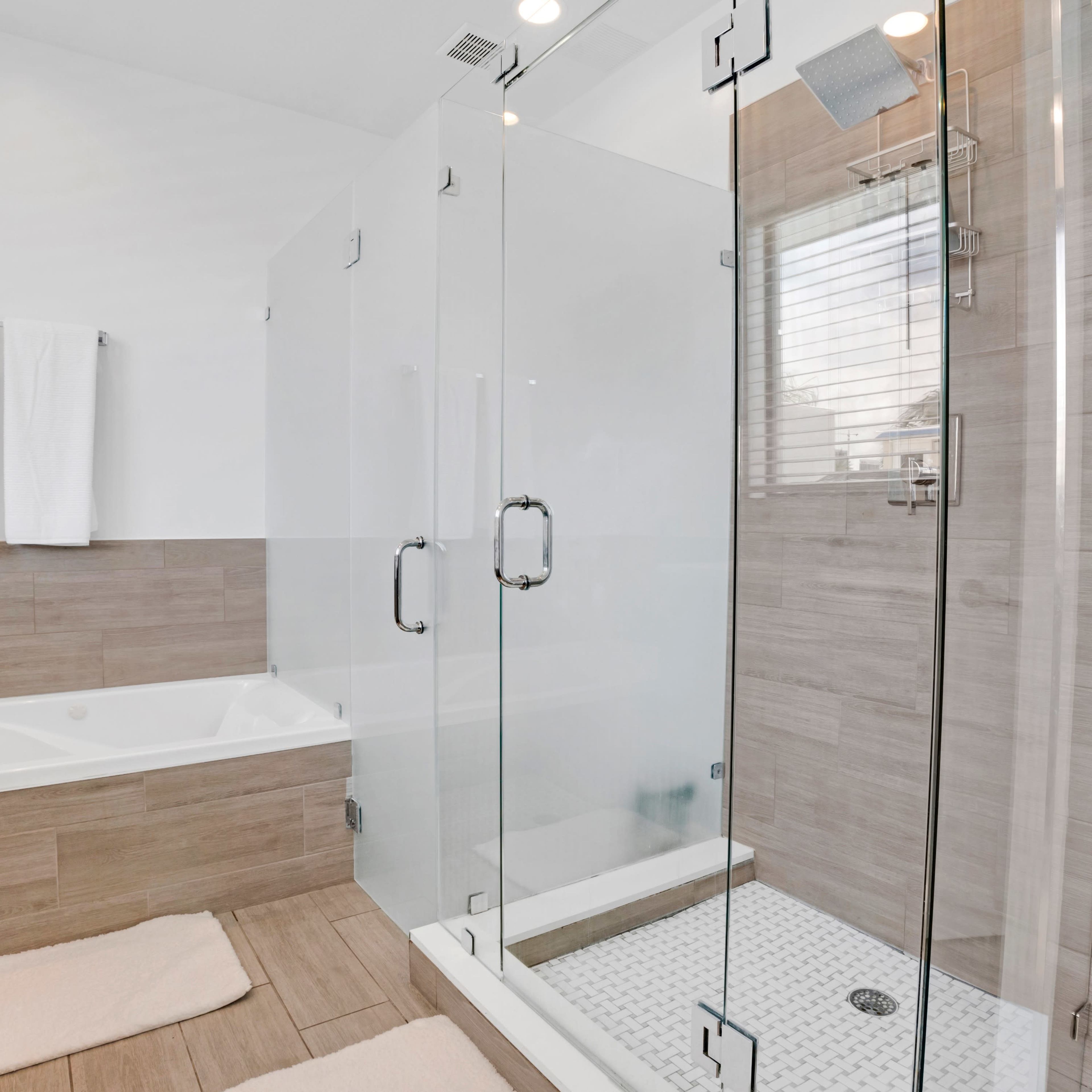 A modern bathroom with a glass-enclosed shower, a bathtub, and light-colored tile flooring.