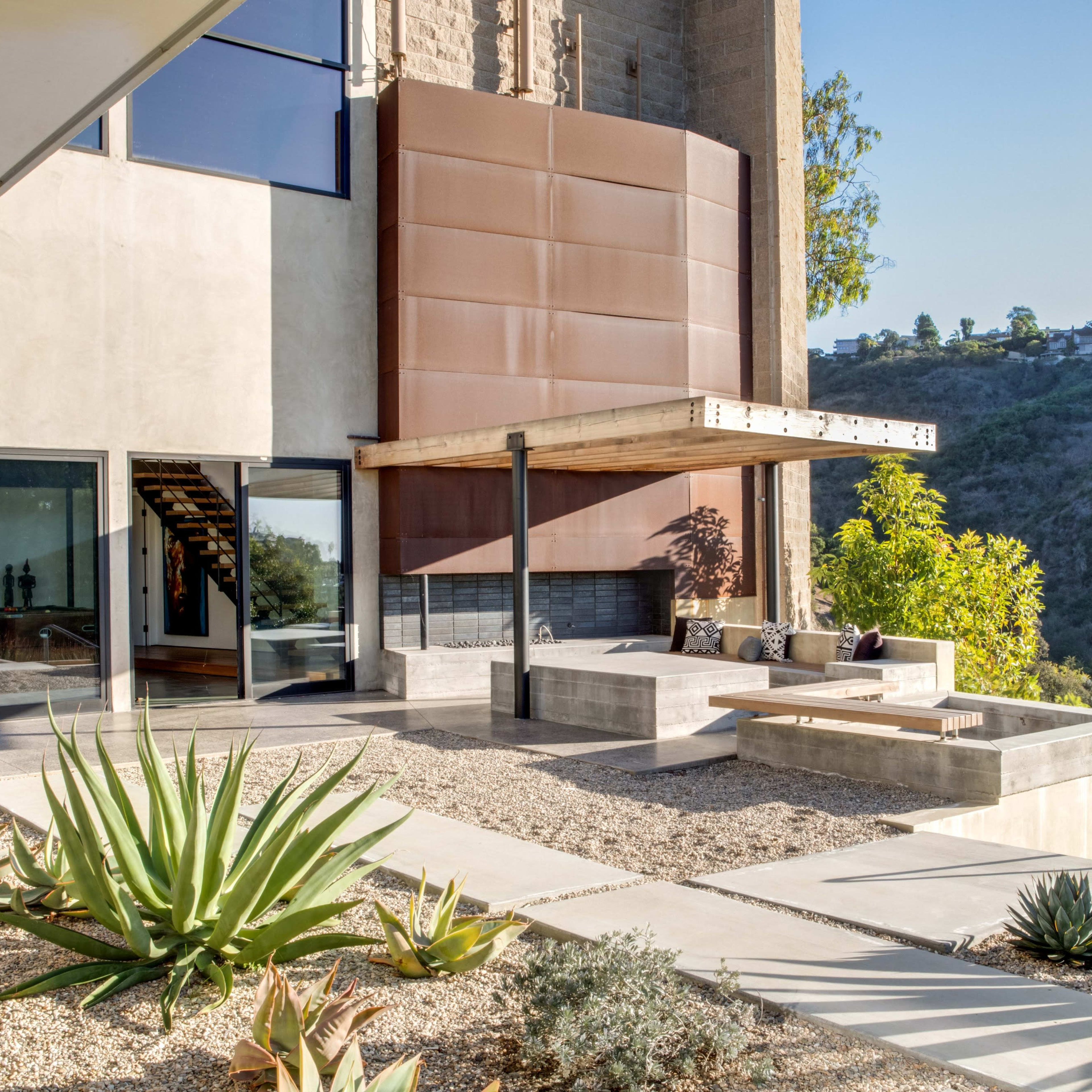 A modern patio area with a wooden overhang, seating, and landscaped outdoor space featuring succulents and a view of a hillside.