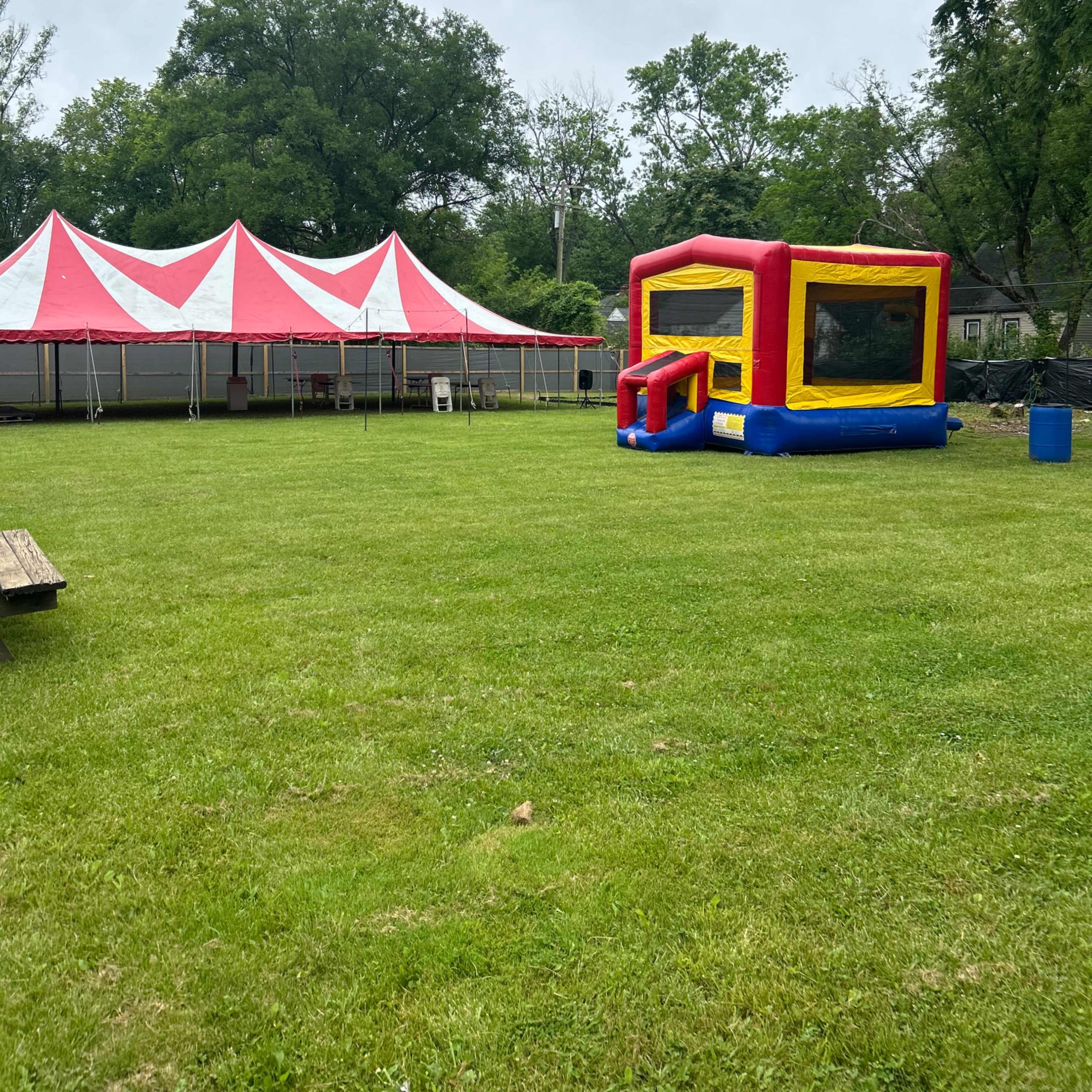 A red and yellow inflatable bounce house sits on a grassy area next to a large red and white striped tent.