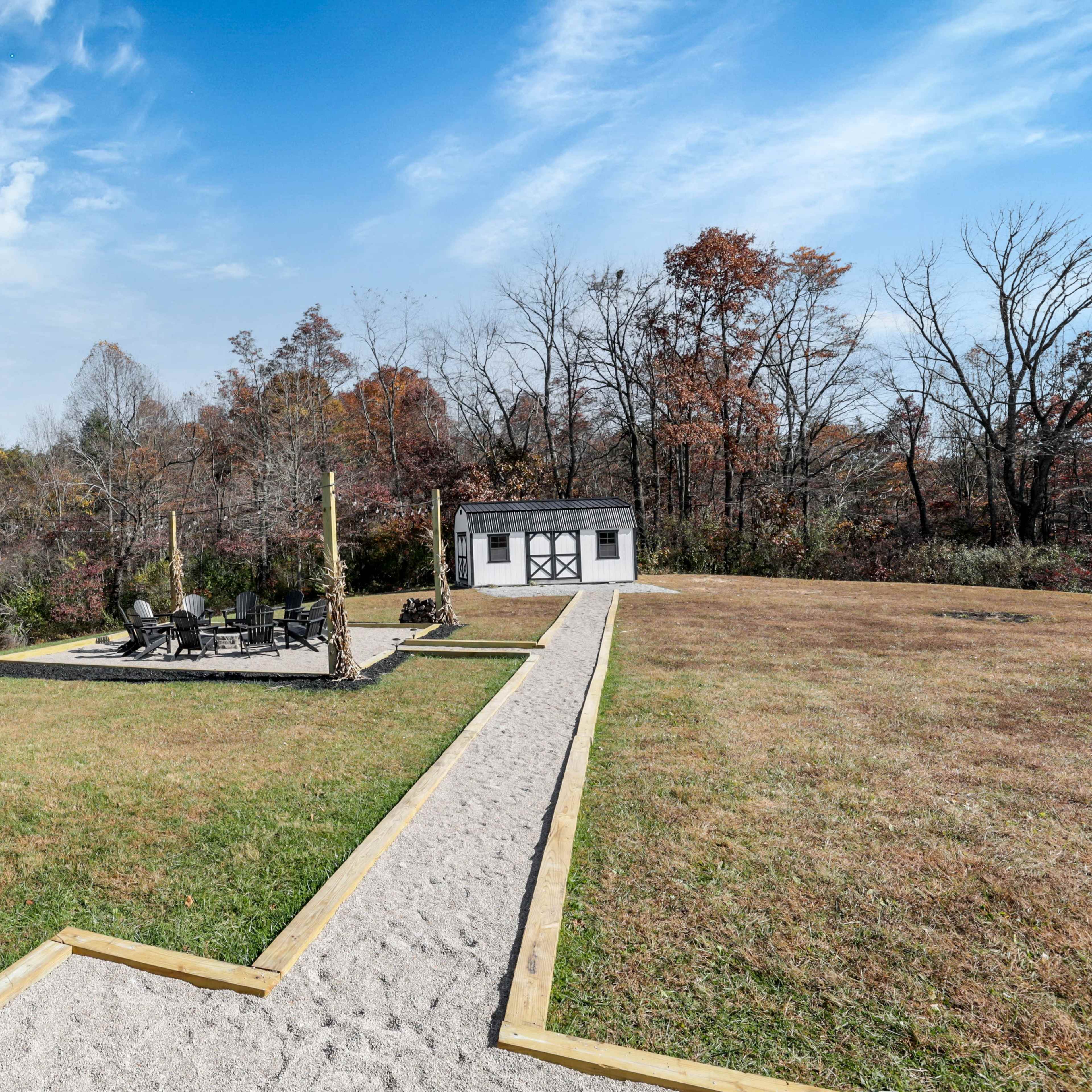 A cleared outdoor space with a gravel pathway leading to a shed, surrounded by autumn foliage and a seating area.