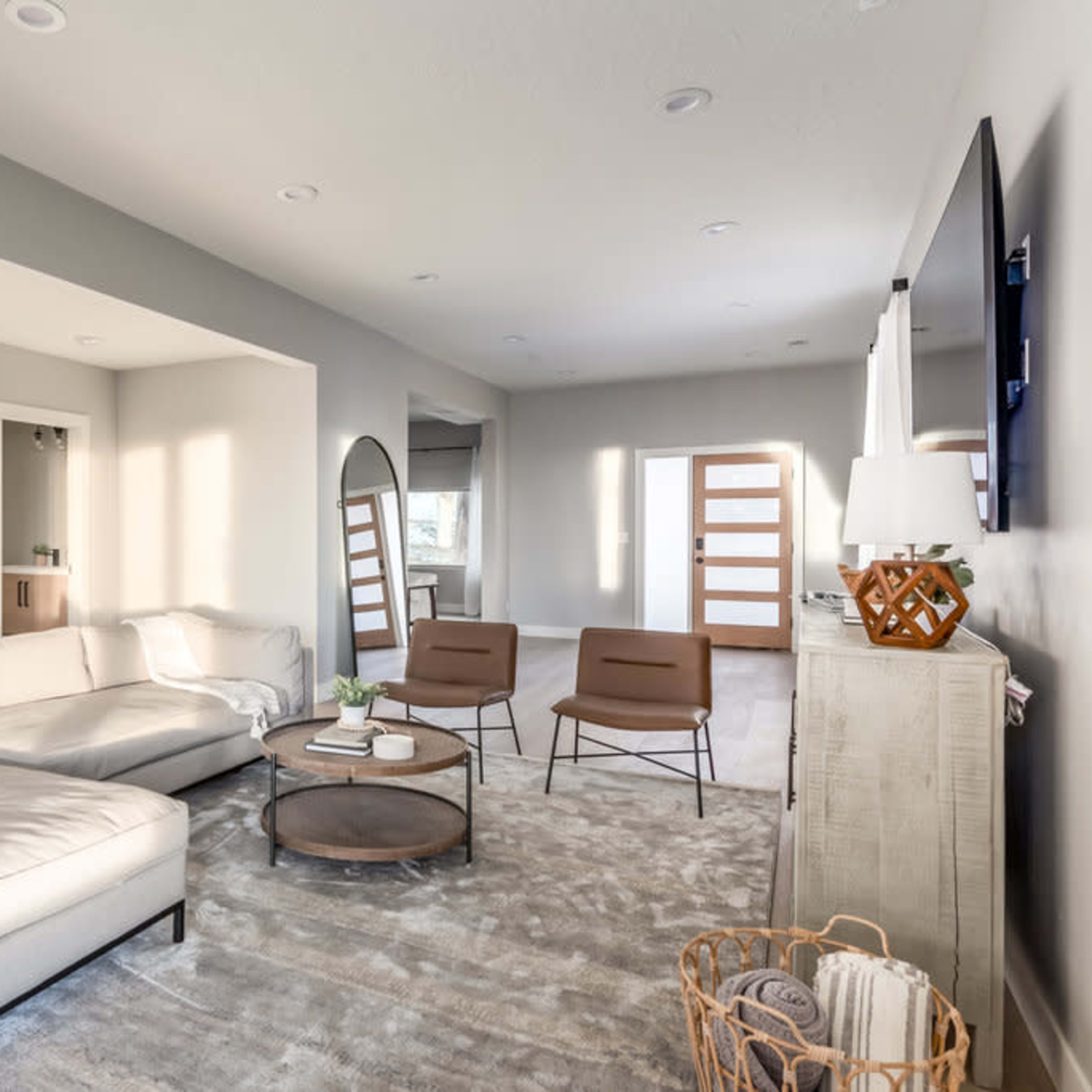 A modern living room with a sectional sofa, two armchairs, a round coffee table, and natural light coming through multiple windows.