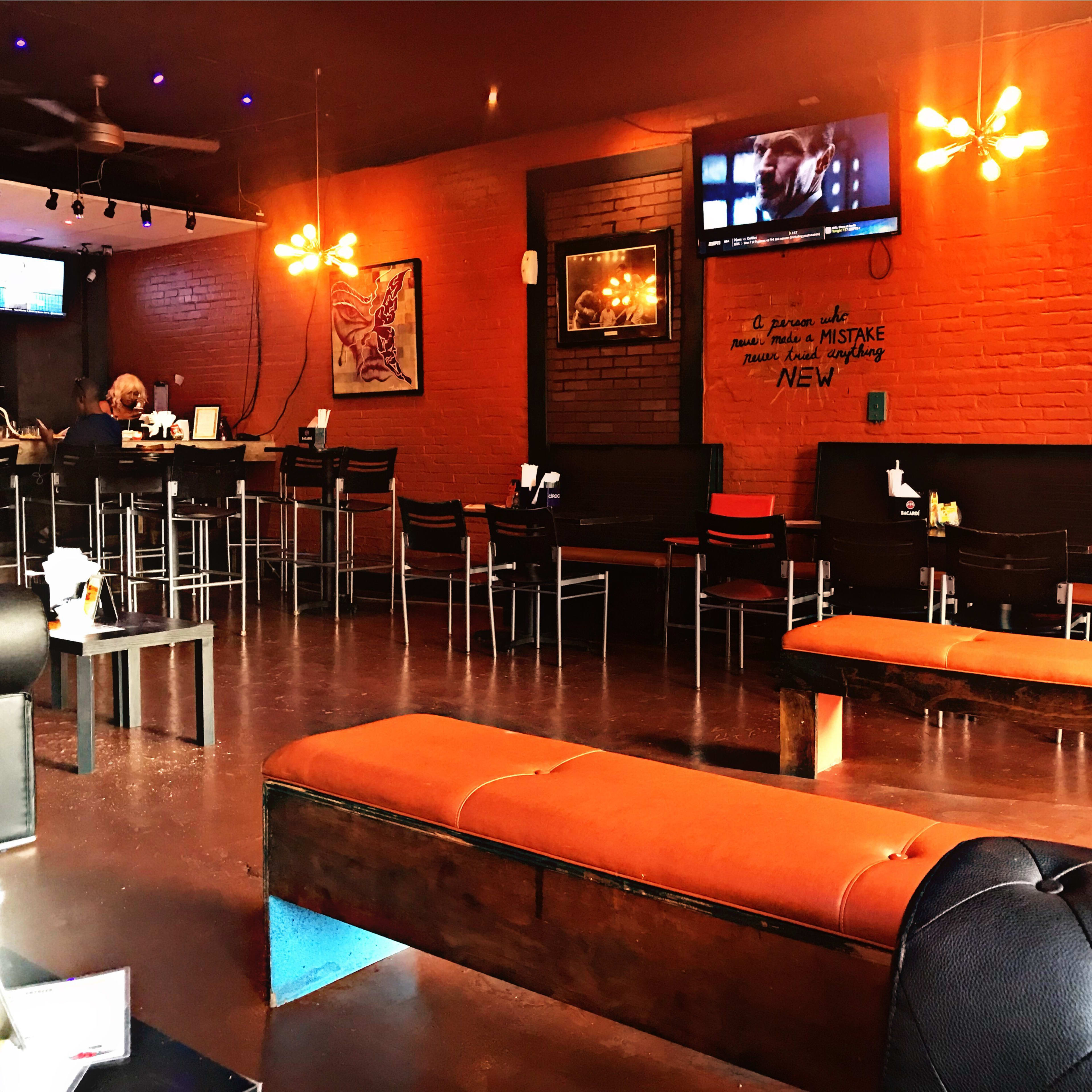 A dimly lit restaurant interior with wooden benches, a bar area, and a television mounted on the wall.