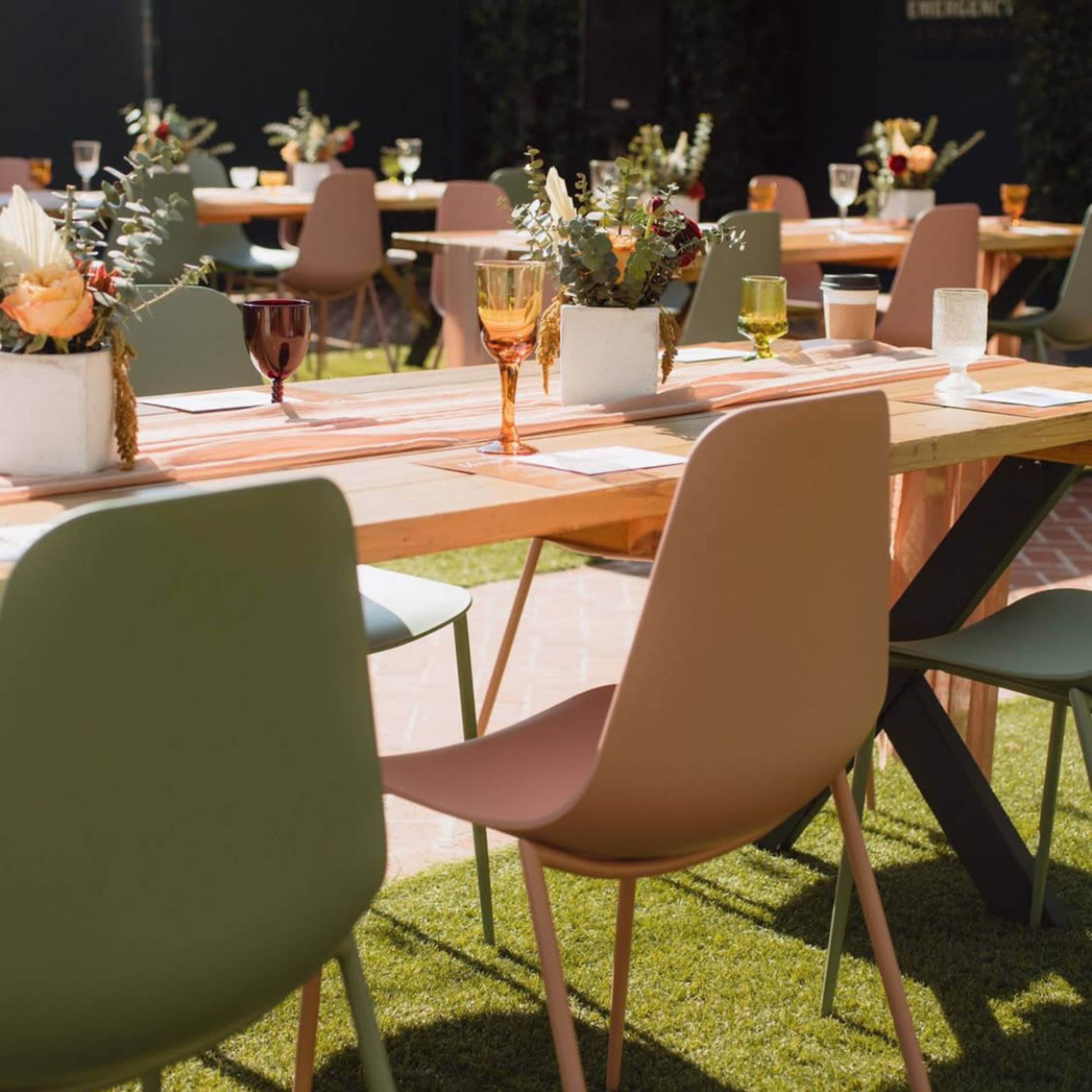 A set of tables adorned with colorful glasses and floral centerpieces is arranged on a grassy area for an outdoor event.