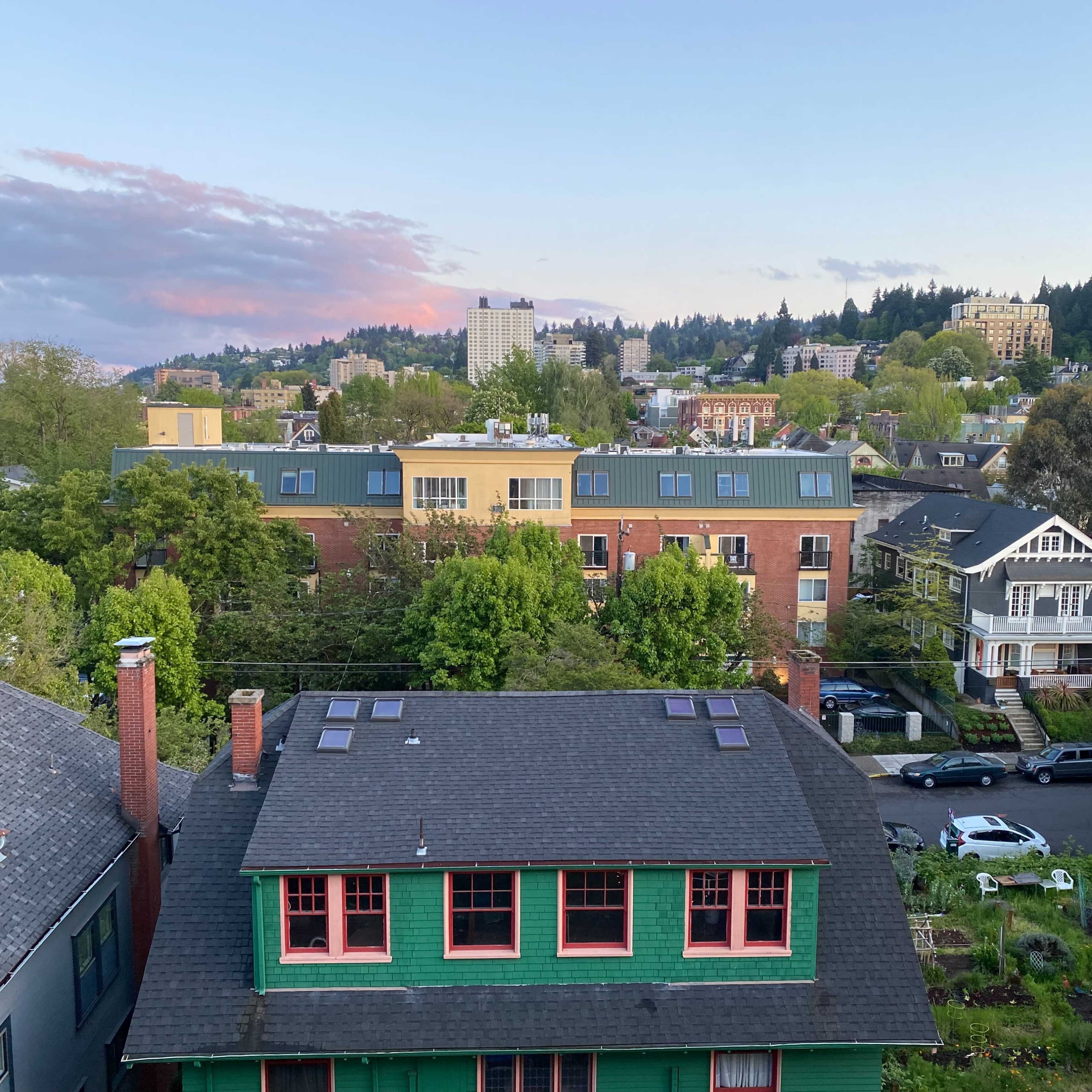 Aerial view of a neighborhood featuring a mix of residential buildings with trees and distant hills under a twilight sky.